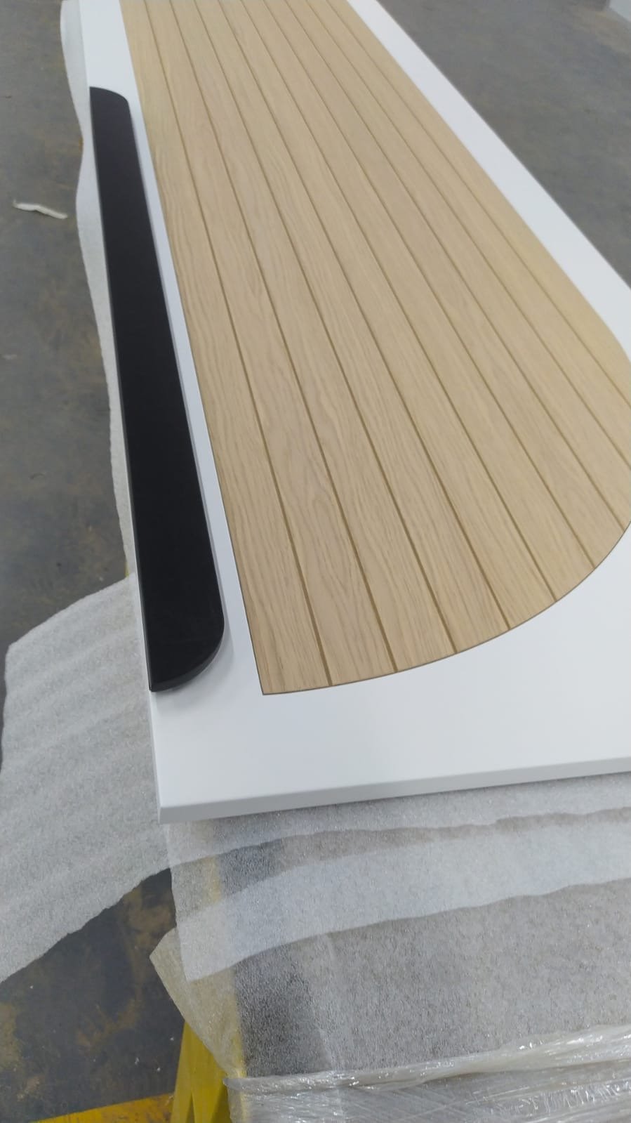 Table en bois clair avec une rallonge en forme de demi-cercle, sur une surface blanche avec un rebord noir.