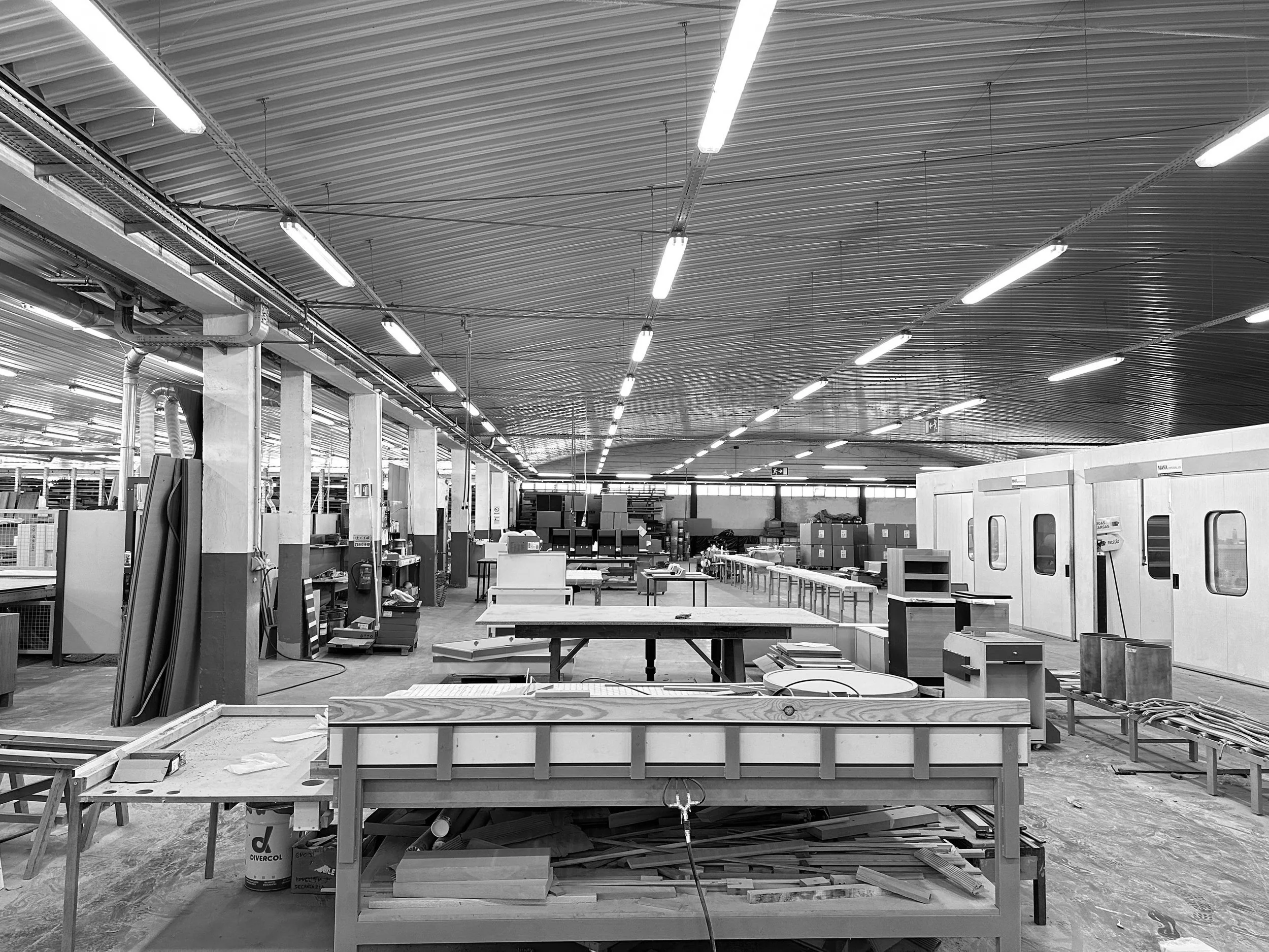 Un atelier de menuiserie ou d'ébénisterie avec des tables de travail, des matériaux en bois et des équipements, dans un espace industriel spacieux.