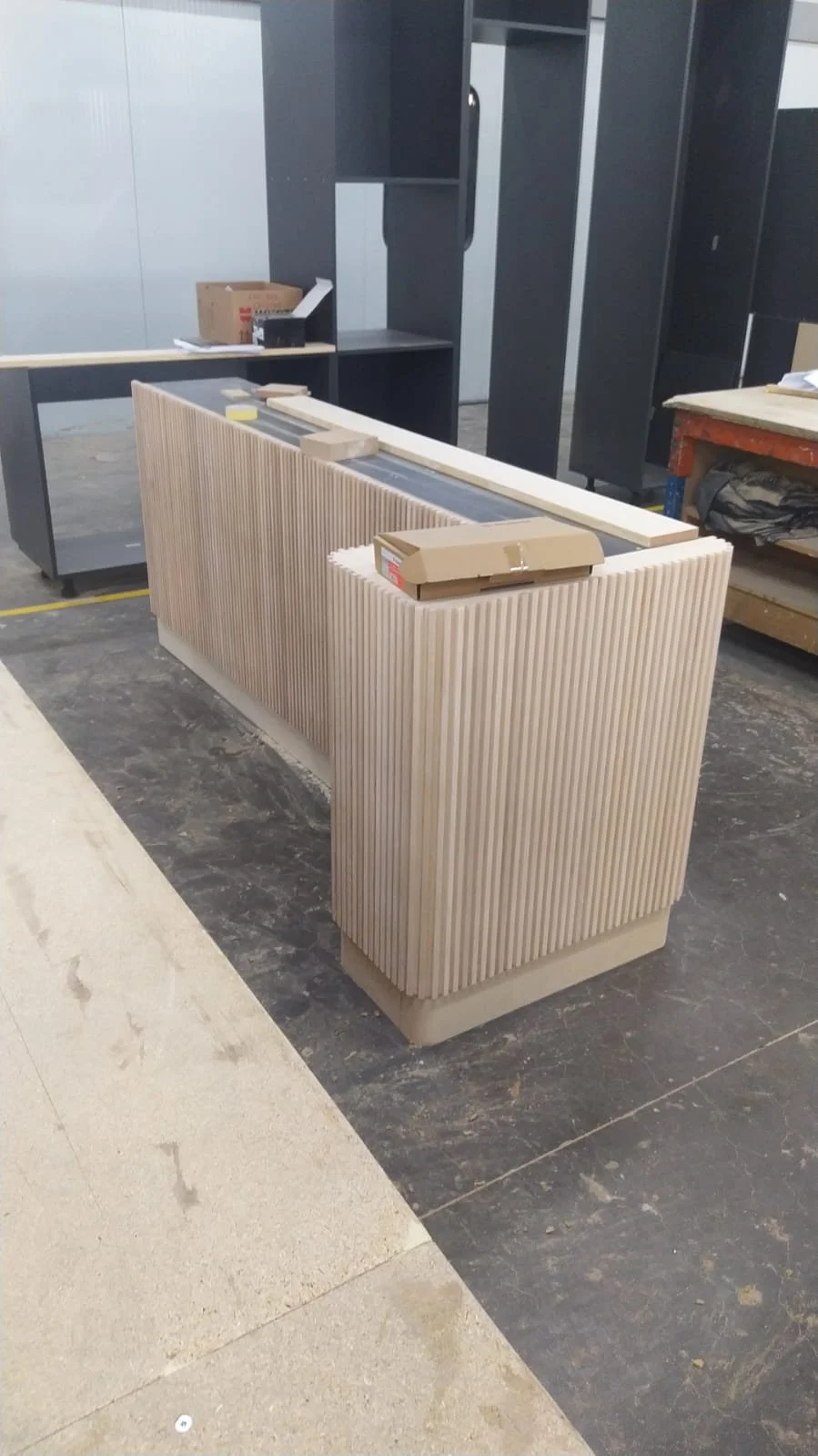 Meuble en cours de fabrication dans un atelier, en bois clair avec une finition rainurée verticale, avec des outils et pièces sur un plan de travail.