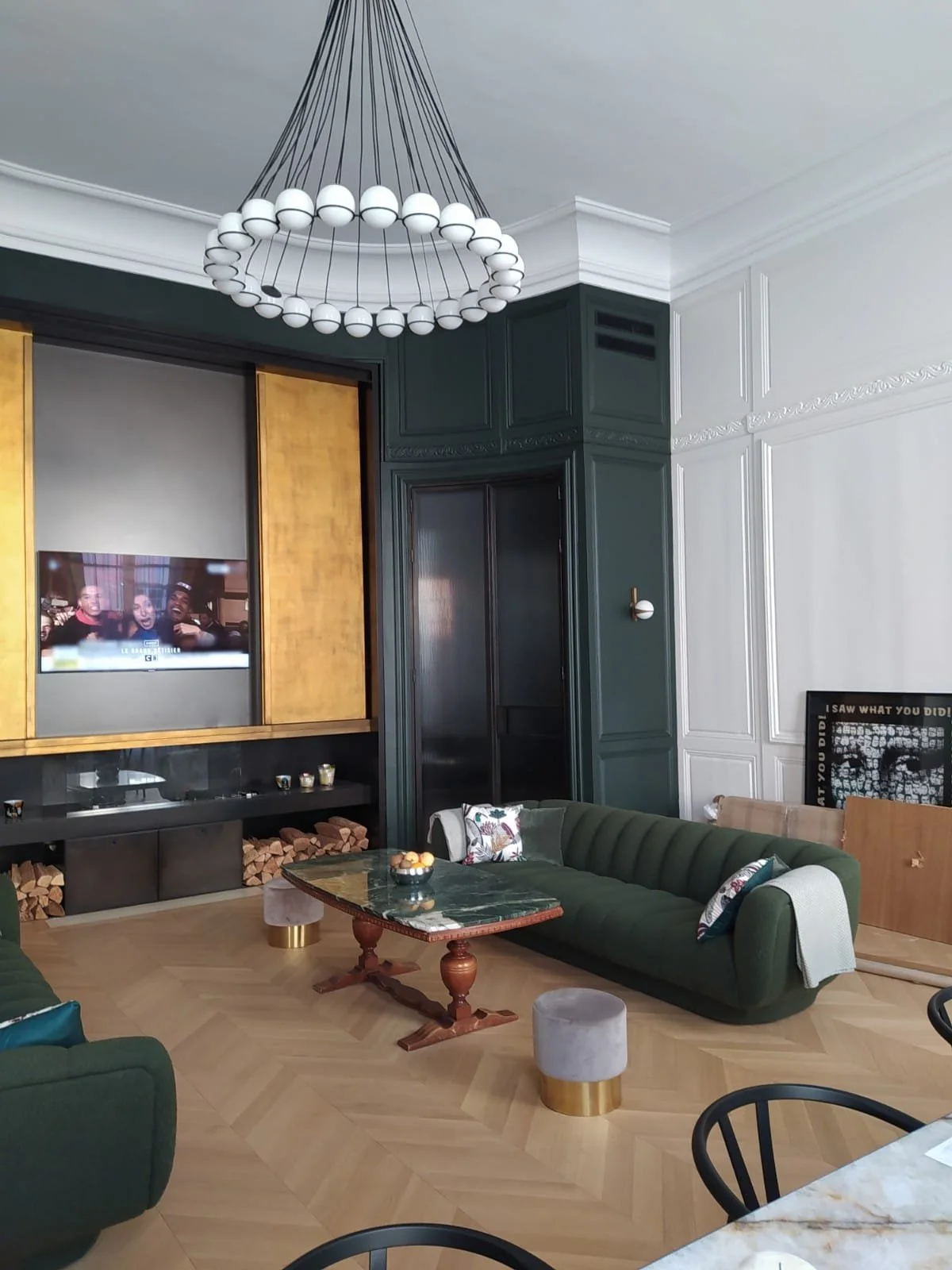 Salon avec canapé vert, table en marbre, télévision, et cheminée, décoration moderne et lumineuse.