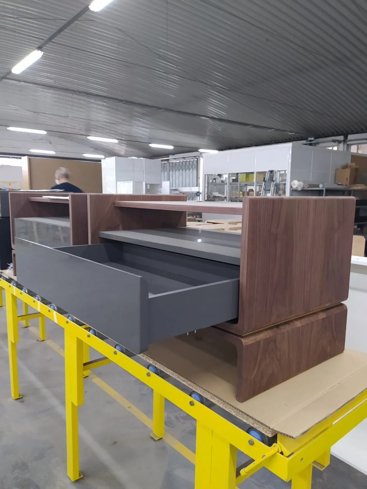 Mobilier de bureau en cours d'assemblage dans une usine, avec un mobilier en bois foncé, en gris et en métal, placé sur un support jaune.