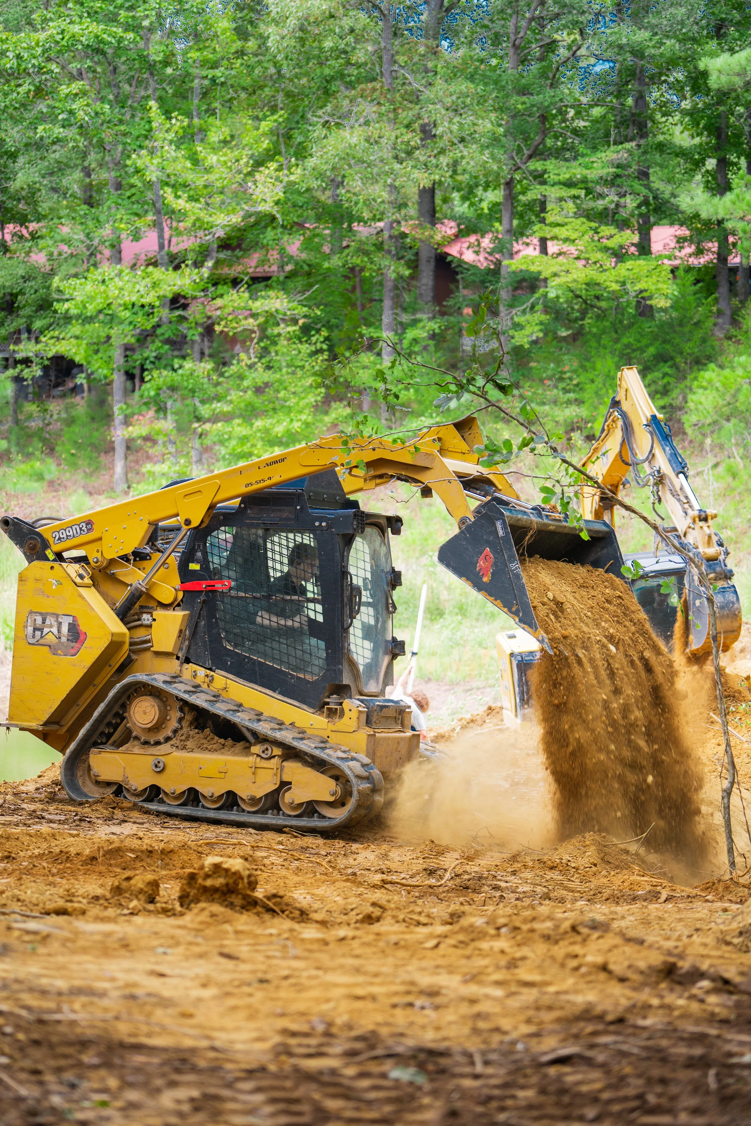 A yellow bulldozer digging and moving dirt on a construction site surrounded by green trees.
