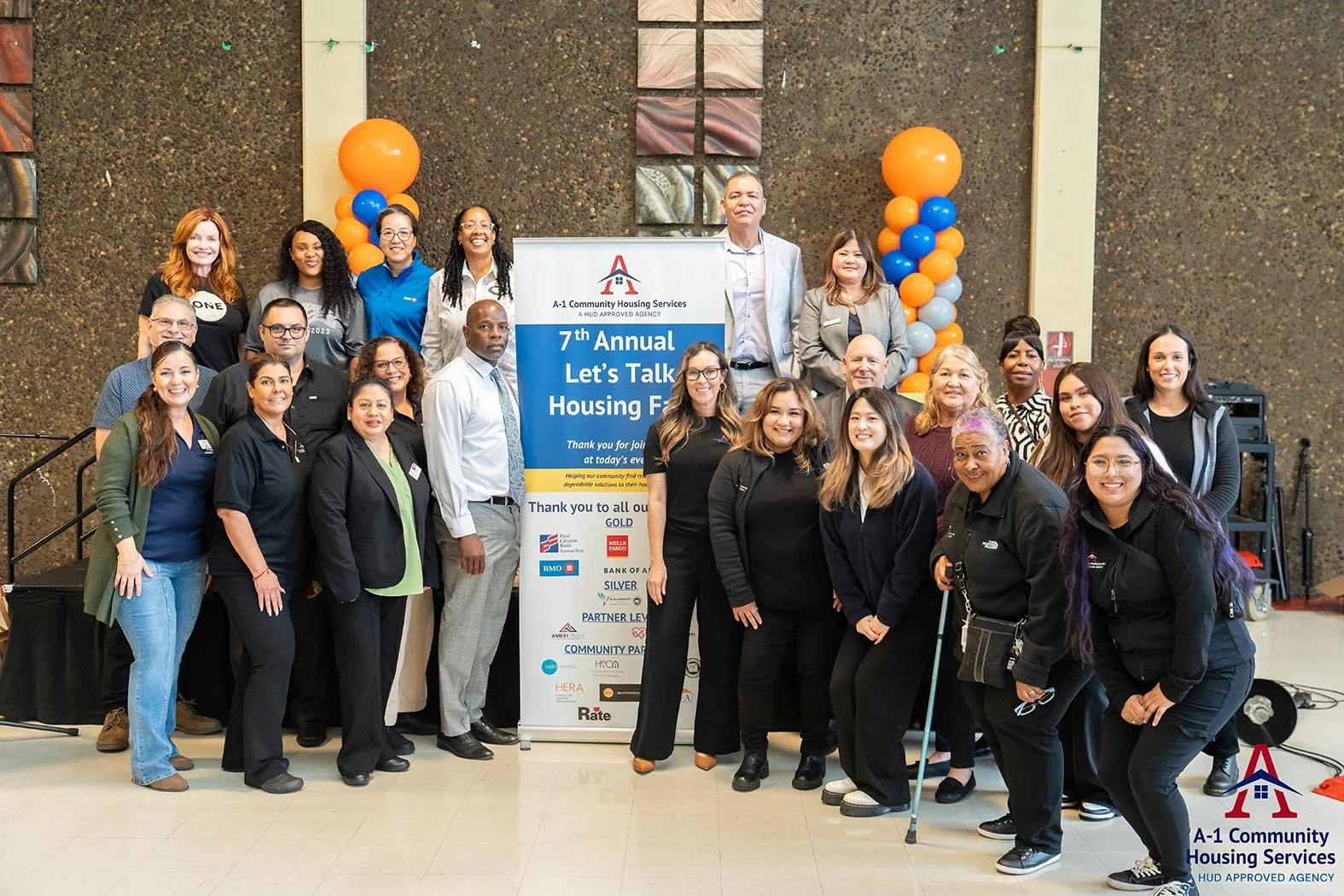 a-1-community-housing-services-staff-and-volunteers-smiling-for-a-group-photo-while-standing-around-a-banner-that-says-7th-annual-lets-talk-housing-fair.jpg