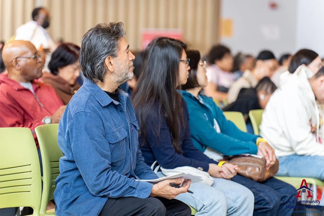 family-sitting-together-in-an-auditorium-full-of-other-community-members-listening-to-a-presentation-on-housing.jpg