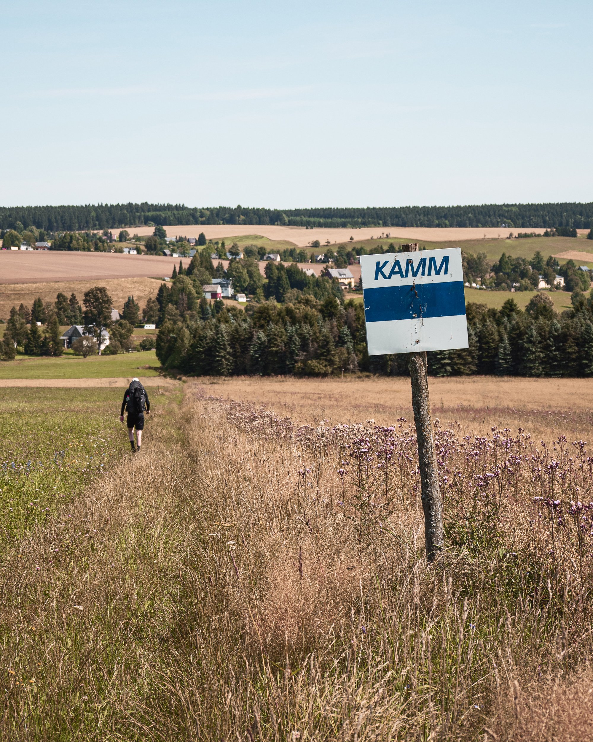 Backpacker hiking along the Kamm trail through open rural fields with expansive countryside views.