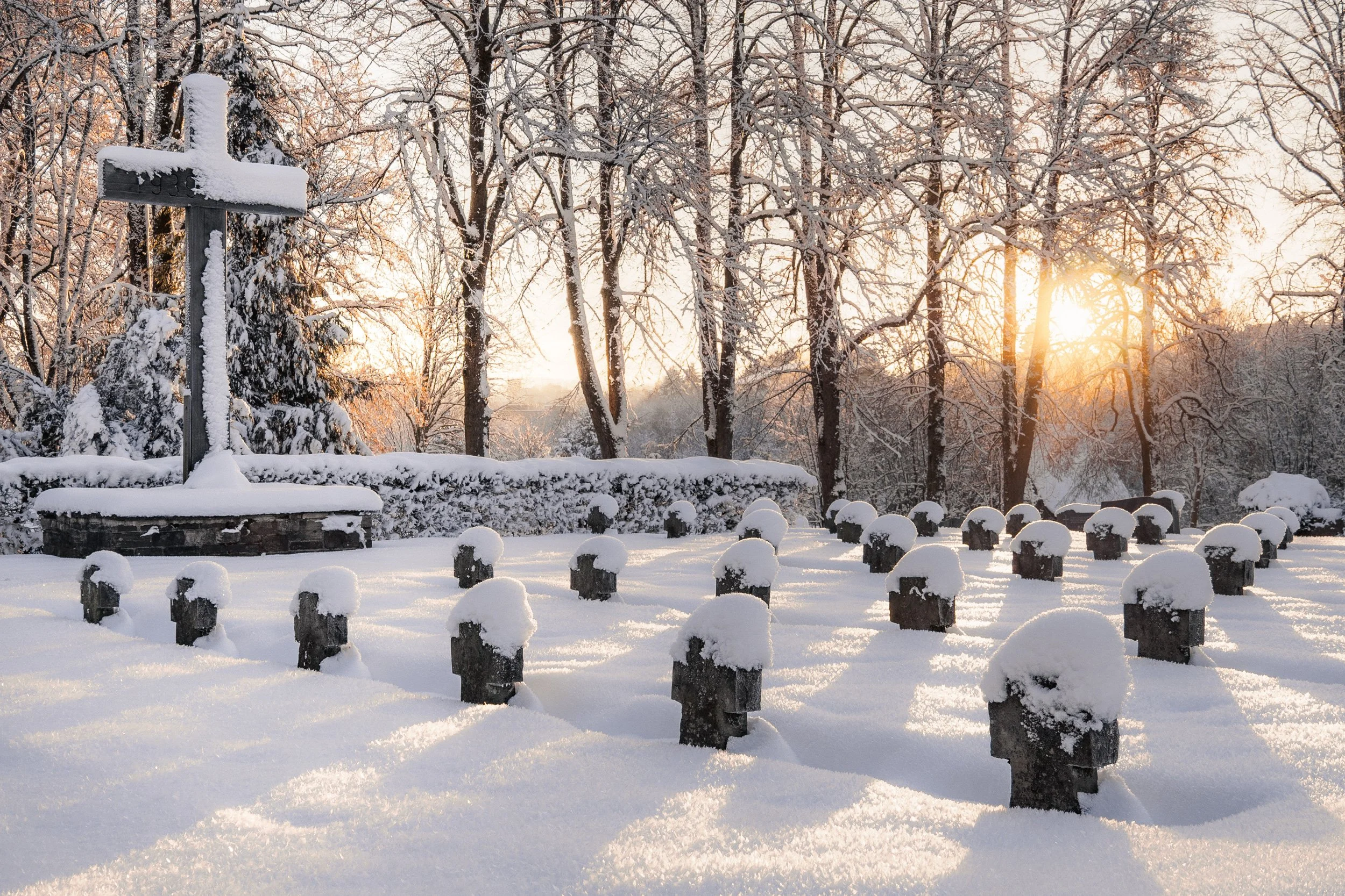 Snow-covered military cemetery at sunrise with warm golden light illuminating rows of historic grave markers.