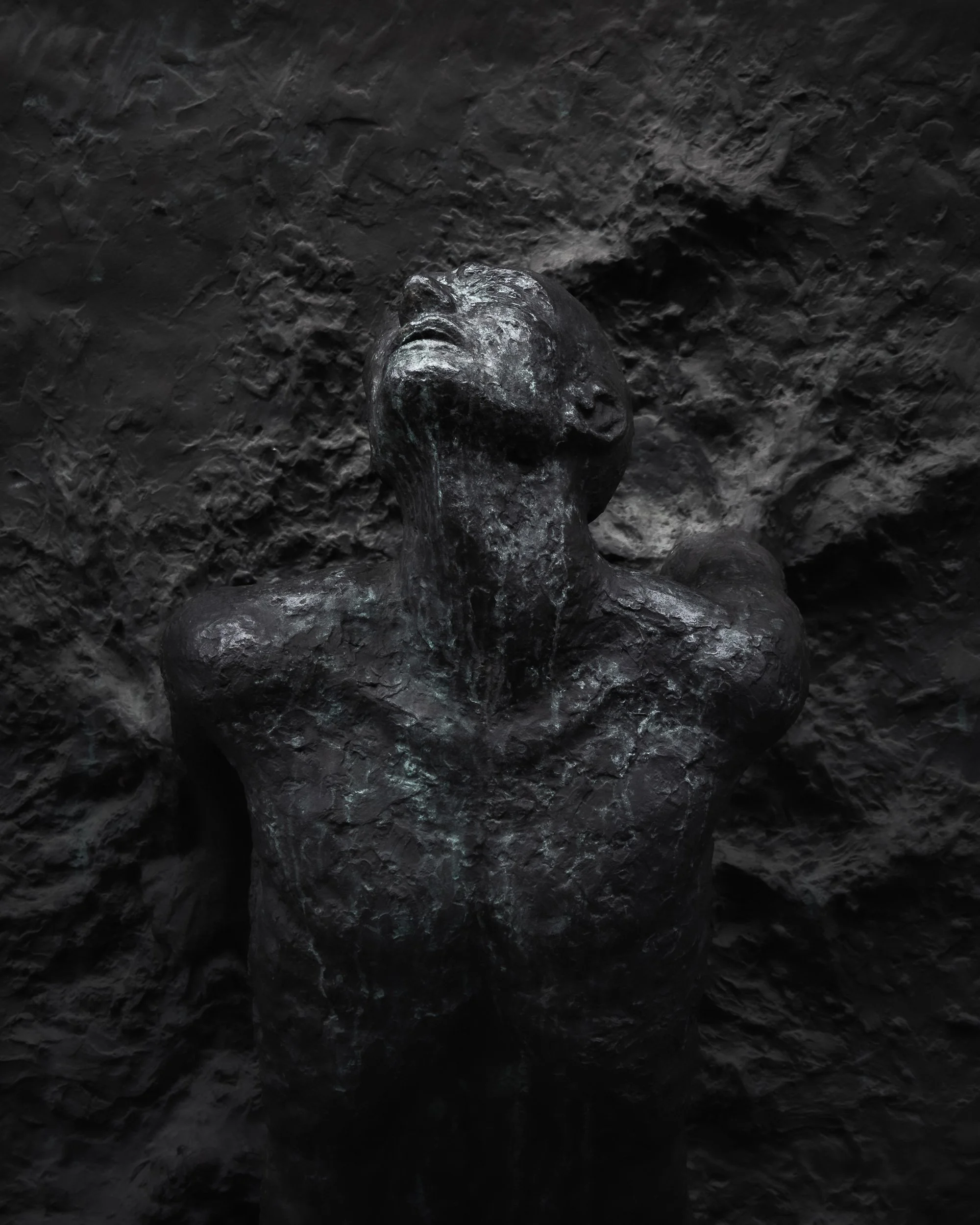 Dark abstract bronze sculpture of a human figure emerging from textured stone, expressive fine art photography.