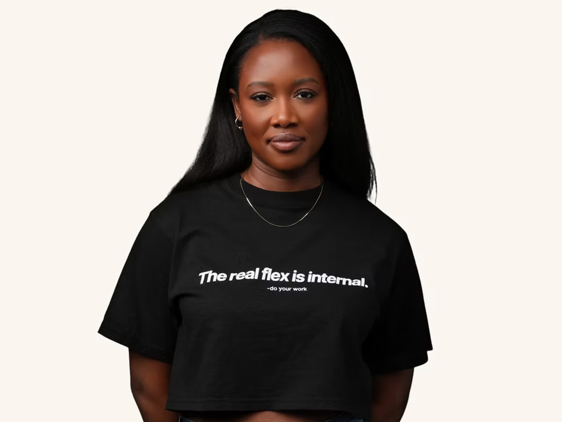 A Black woman with long black hair, wearing a black crew neck t-shirt with white text that reads 'The real flex is internal. - do your work'.