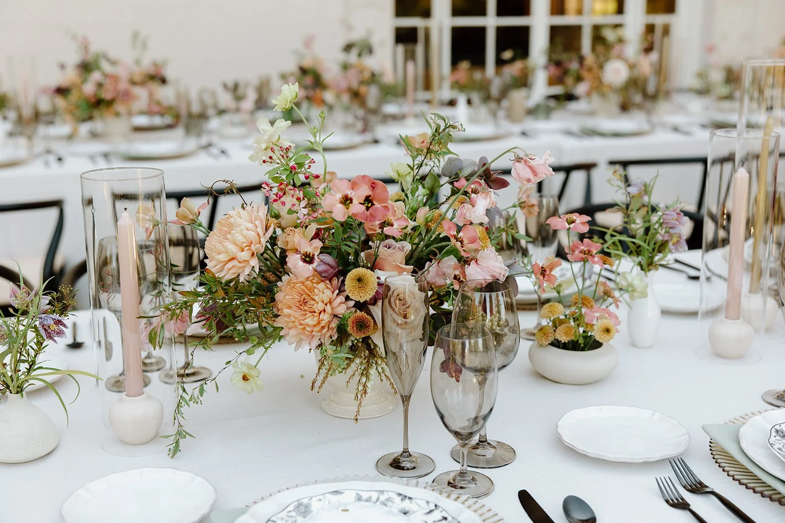 Elegant wedding reception table at Villa Montalvo in Saratoga, California, featuring garden-style floral arrangements of dahlias, roses, and sweet peas in pastel tones, accented with taper candles.