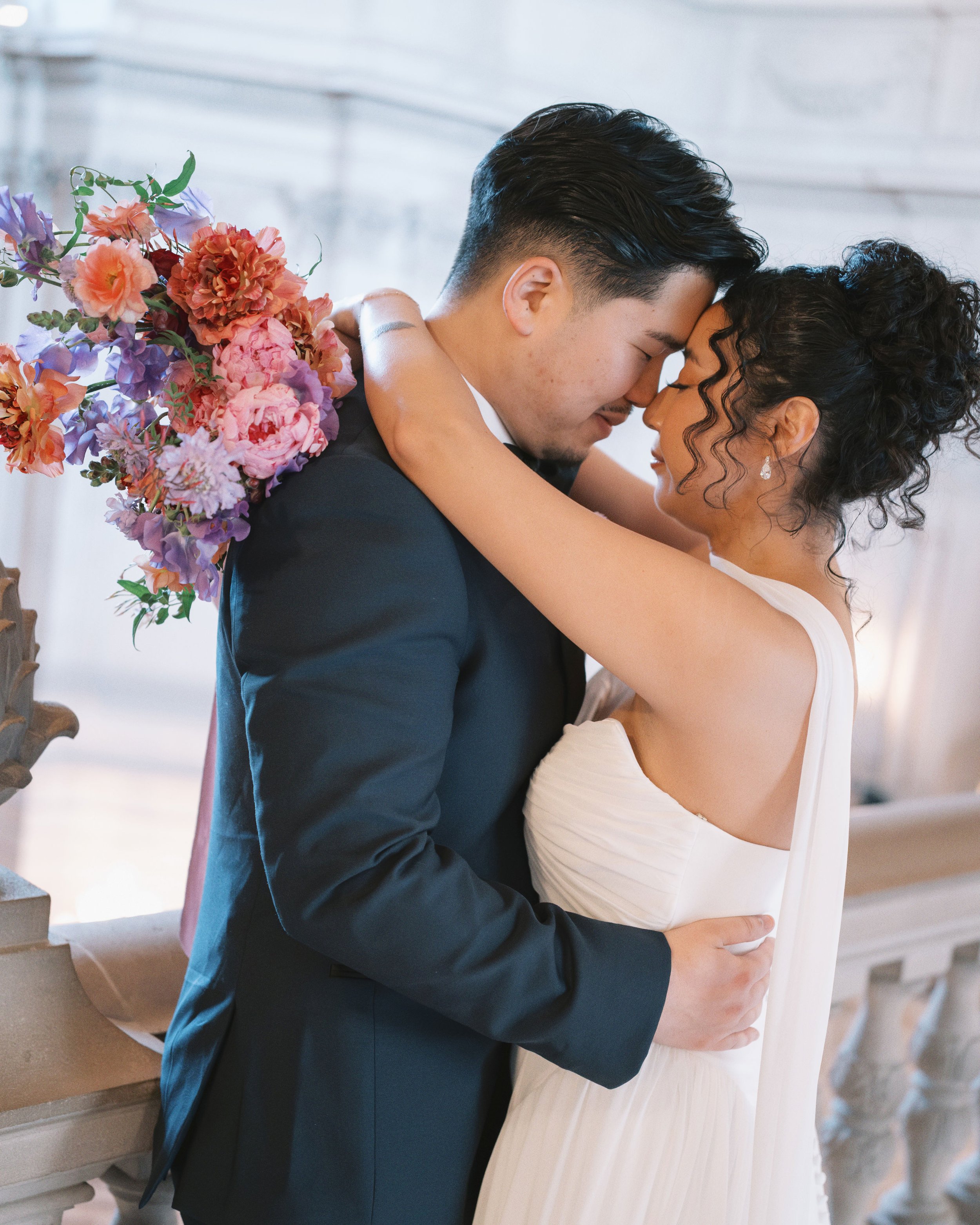 Bride and groom in a close embrace during their wedding, bride holding a colorful bouquet by Petal + Salt Floral