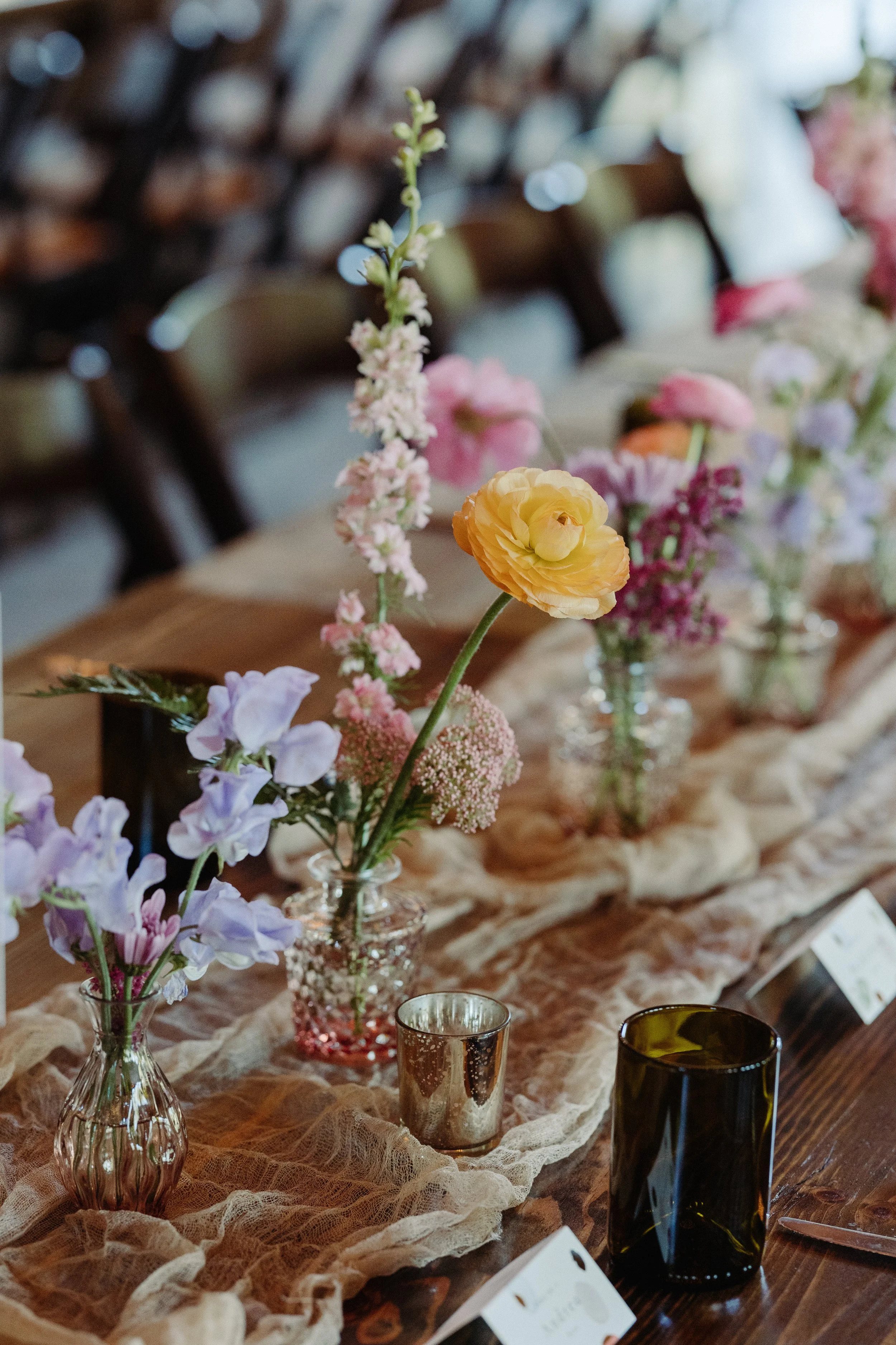Wedding reception tablescape with colorful bud vases, candles, and linen runner, by Petal + Salt Floral