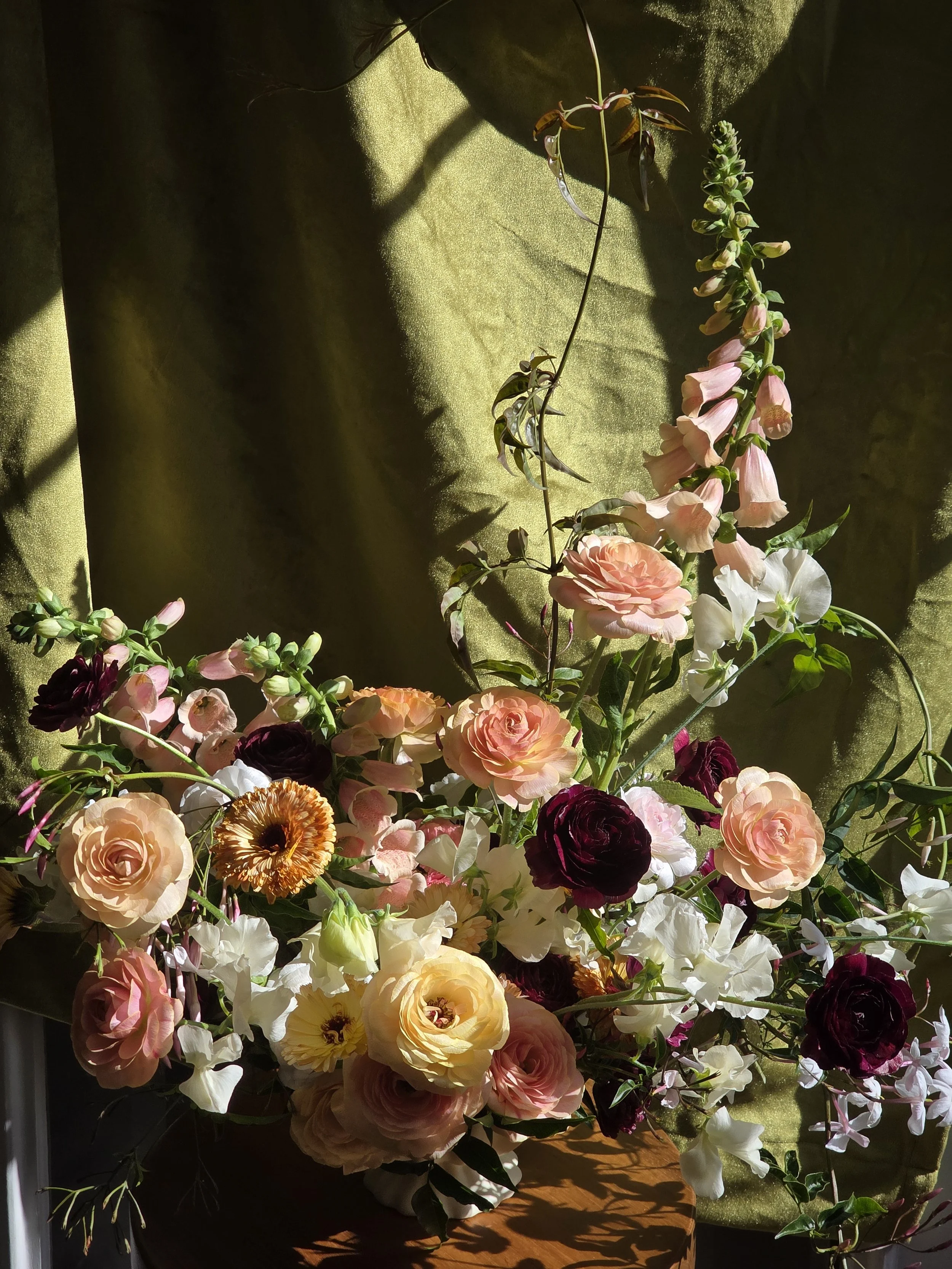 Moody pink, white, and burgundy floral arrangement against a green velvet backdrop, by Petal + Salt Floral