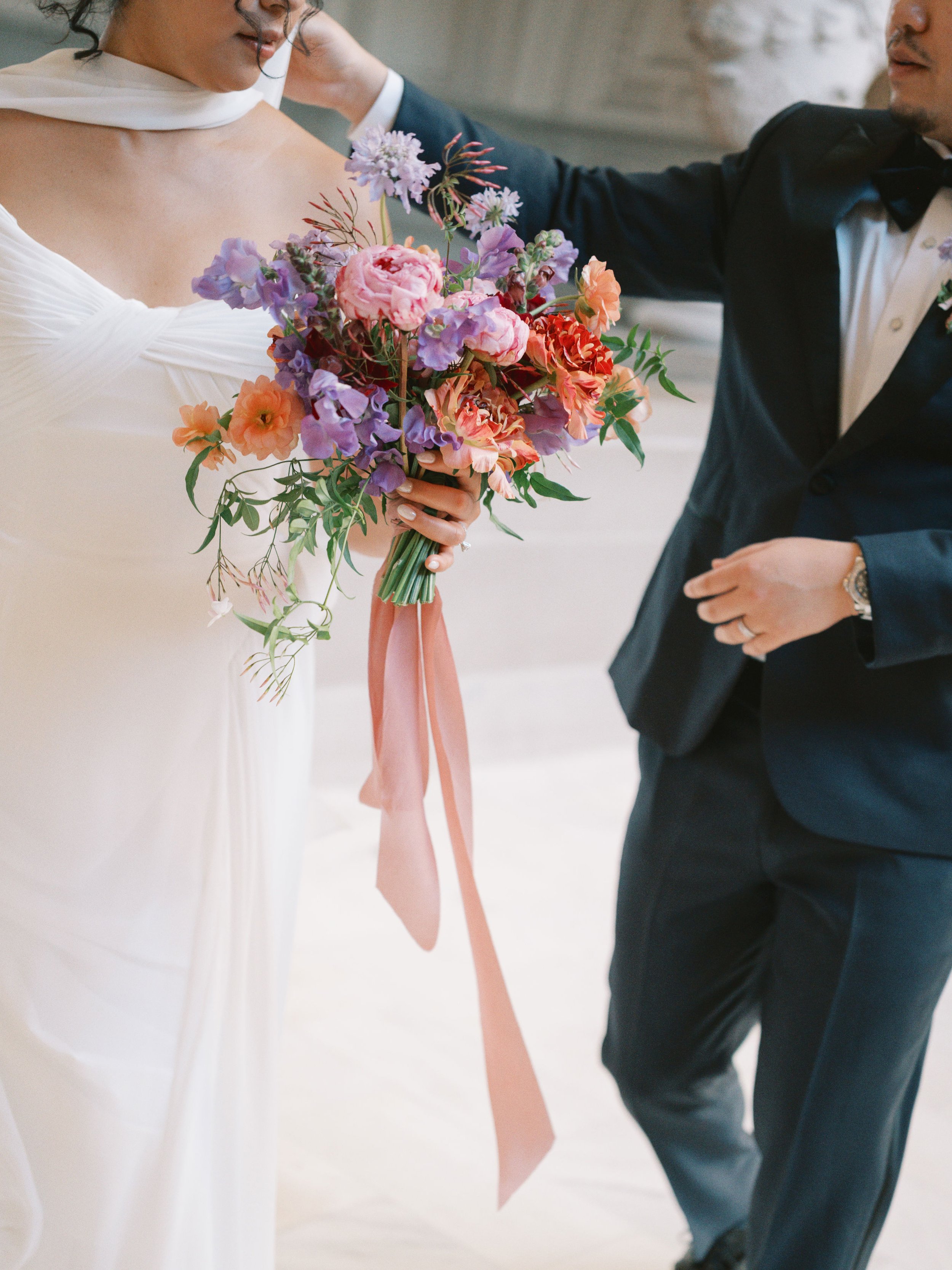 Bride holding a lush colorful bouquet while her partner adjusts her veil, wedding florals by Petal + Salt Floral