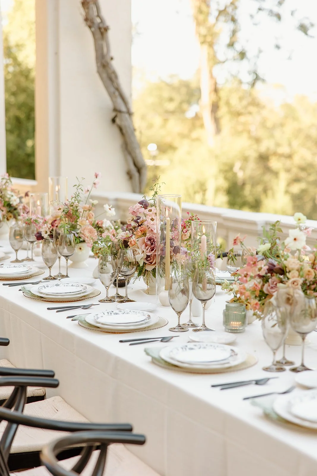 Outdoor wedding reception on the veranda of Villa Montalvo, the table decorated with pink and purple floral centerpieces, candles, and layered place settings, Petal and Salt Floral