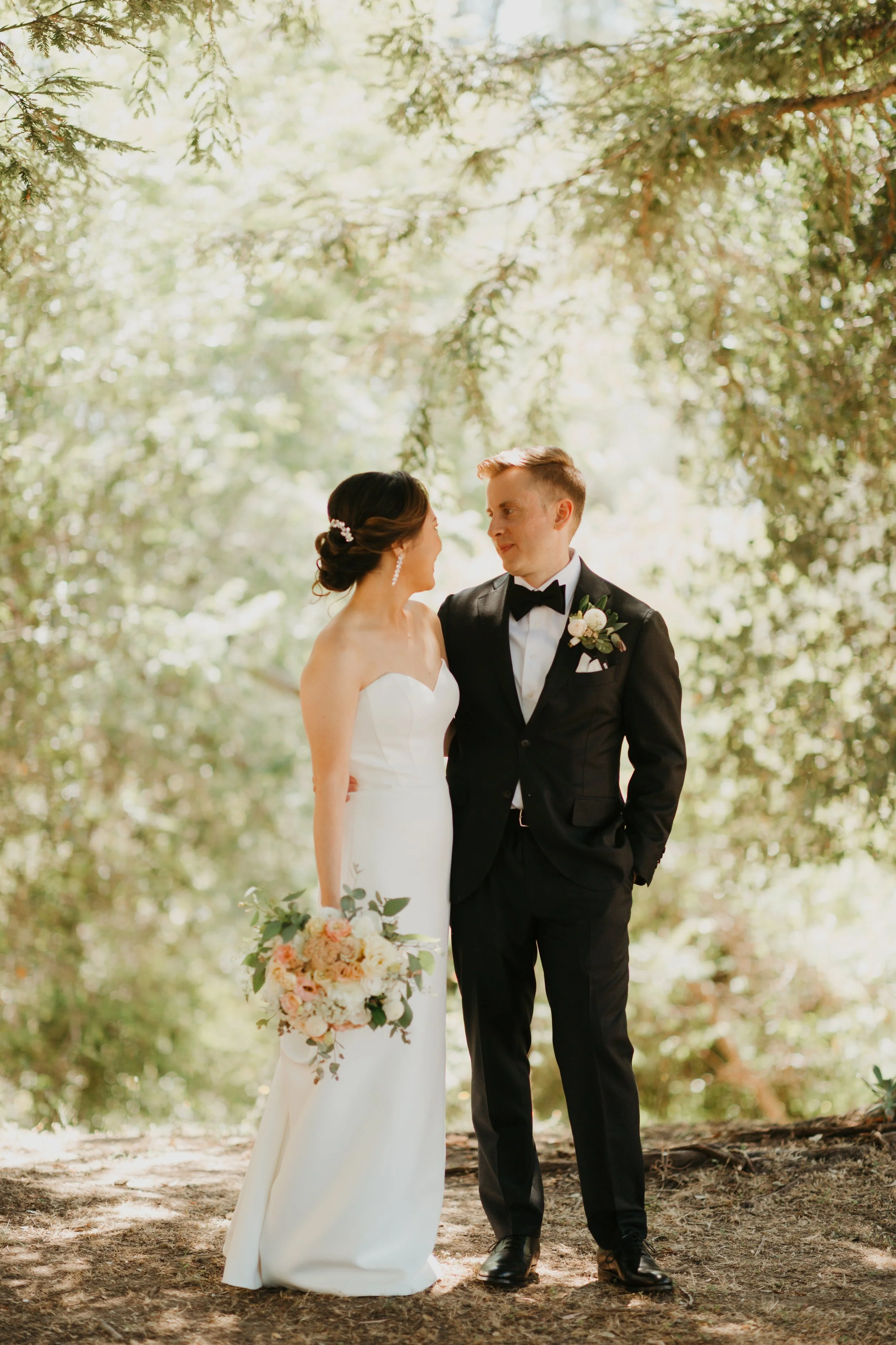 Outdoor wedding ceremony flowers at Chaminade Resort & Spa in Santa Cruz, California, with the bride holding a garden rose bouquet in soft peach and ivory tones, standing beside the groom with a complimentary boutonniere. 