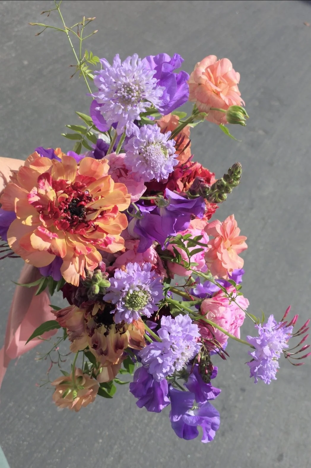 Bold bridal bouquet with purple, peach, pink, and deep red blooms against a dark grey background, designed by Petal and Salt Floral