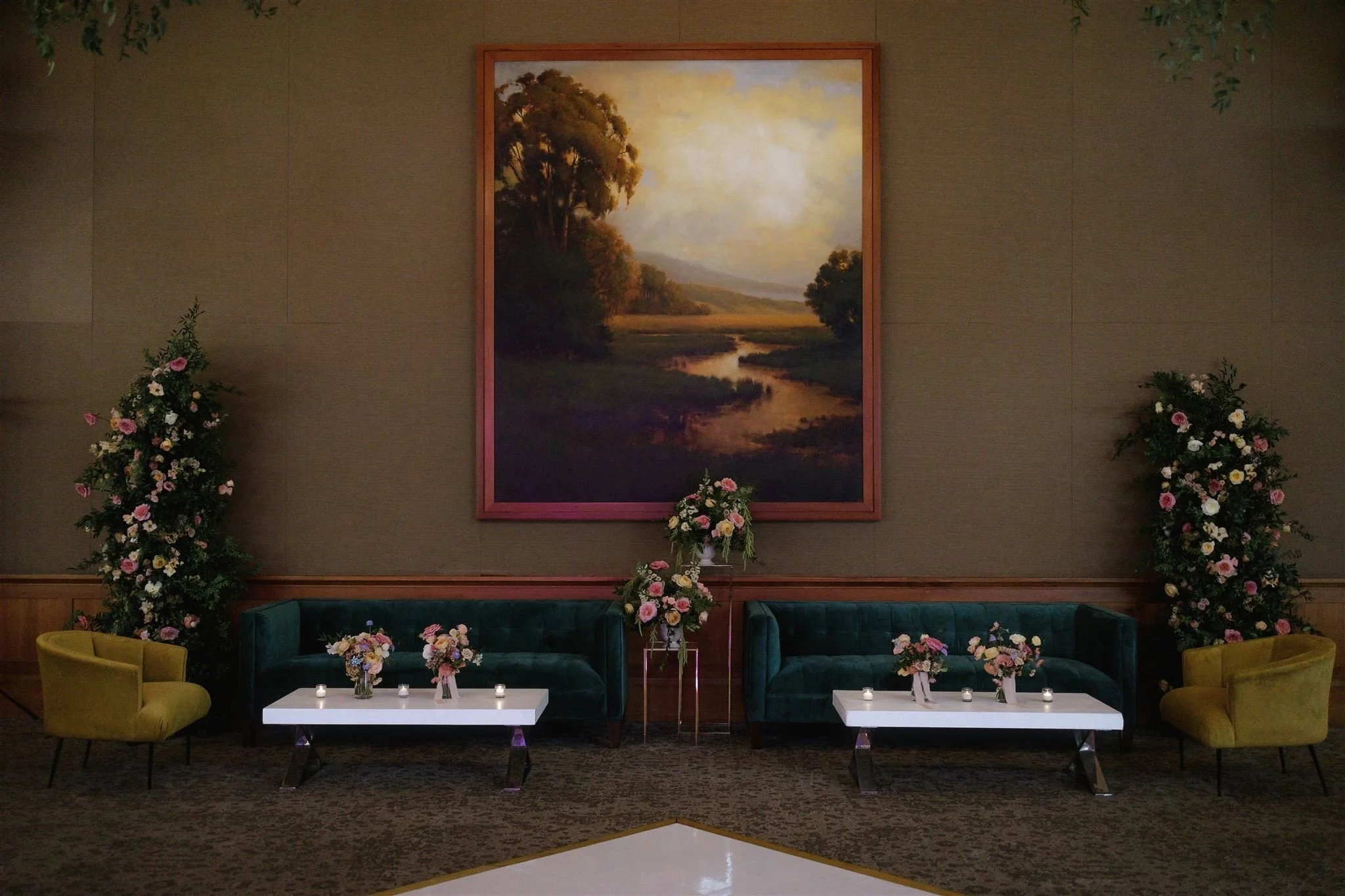 Wedding ceremony flowers repurposed to the lounge at Sharon Heights Country Club in Menlo Park, California, with tall garden-style floral arch of roses and greenery framing the space, accented by romantic welcome arrangements and the beautiful brides