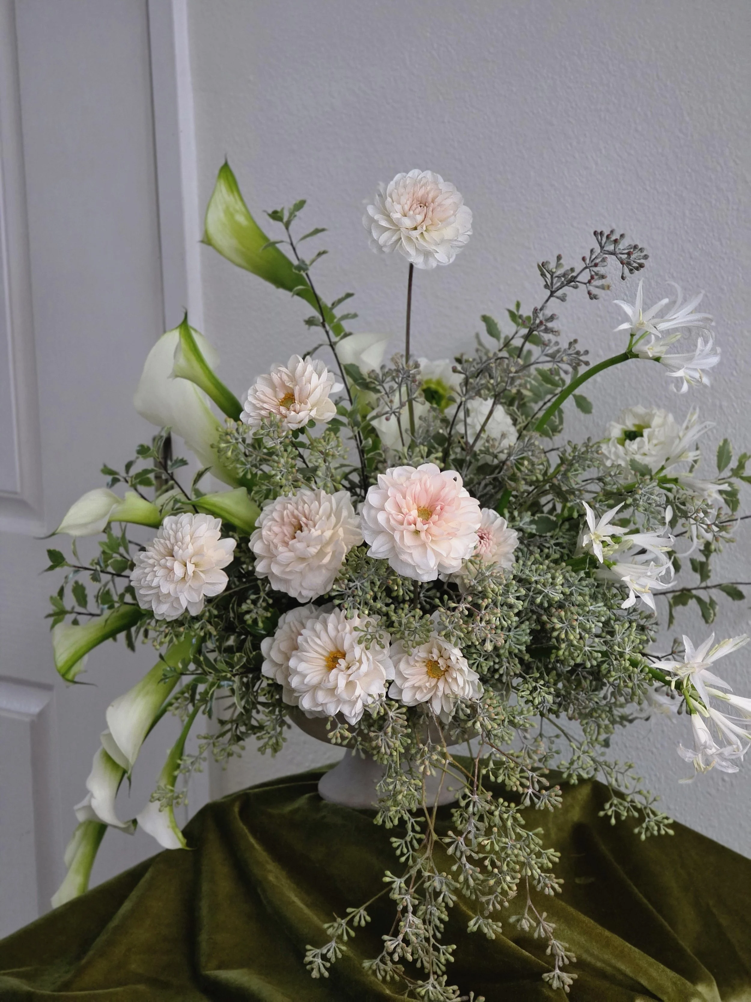 White calla lily's and blush dahlia's with white nerine lilies and seeded eucalyptus in a white vase on dark green velvet, Bay Area wedding florist Petal + Salt