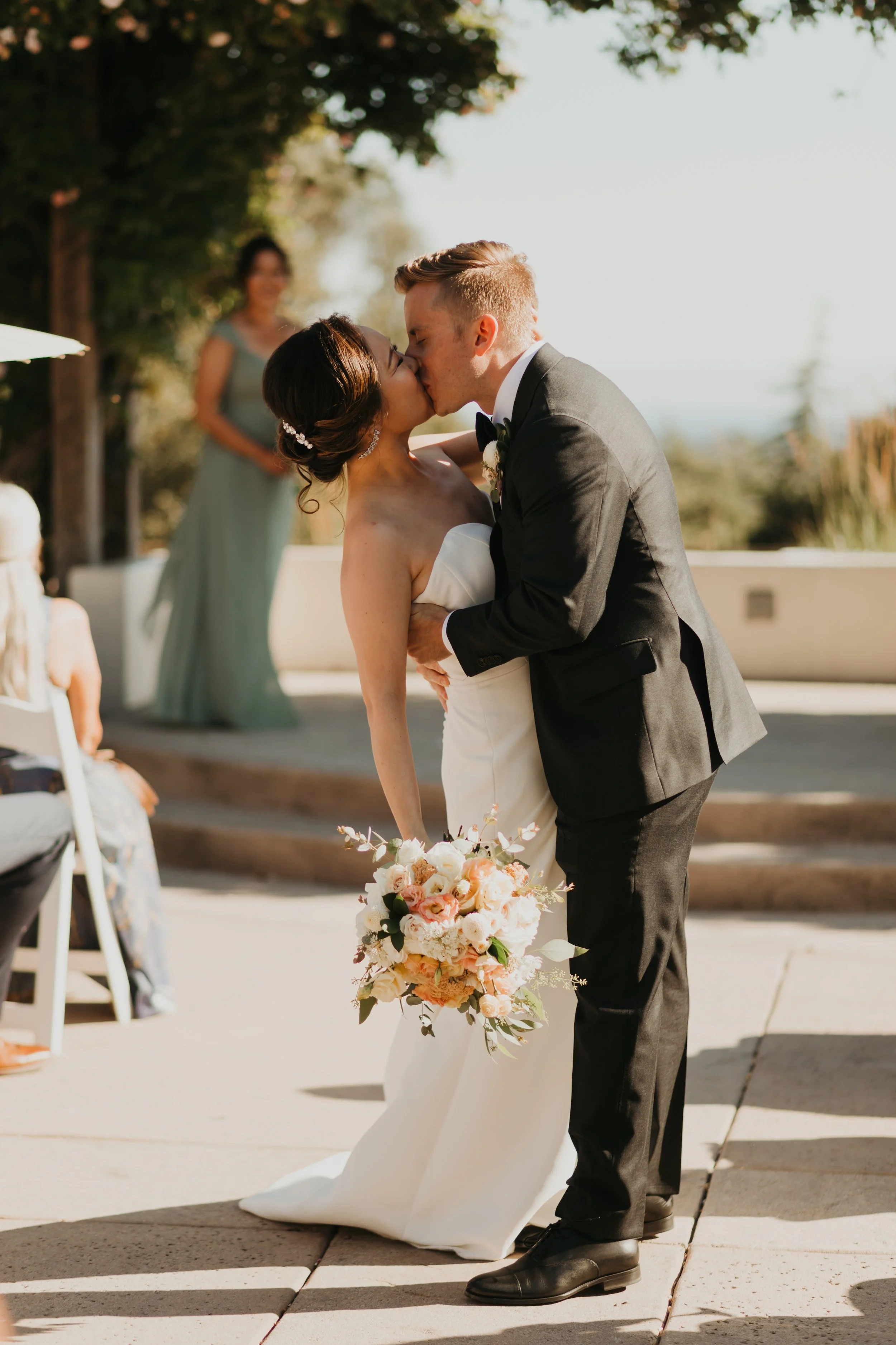 Wedding ceremony at Chaminade Resort & Spa in Santa Cruz, California, with a bride holding a romantic garden rose bouquet as she kisses the groom during their vows.