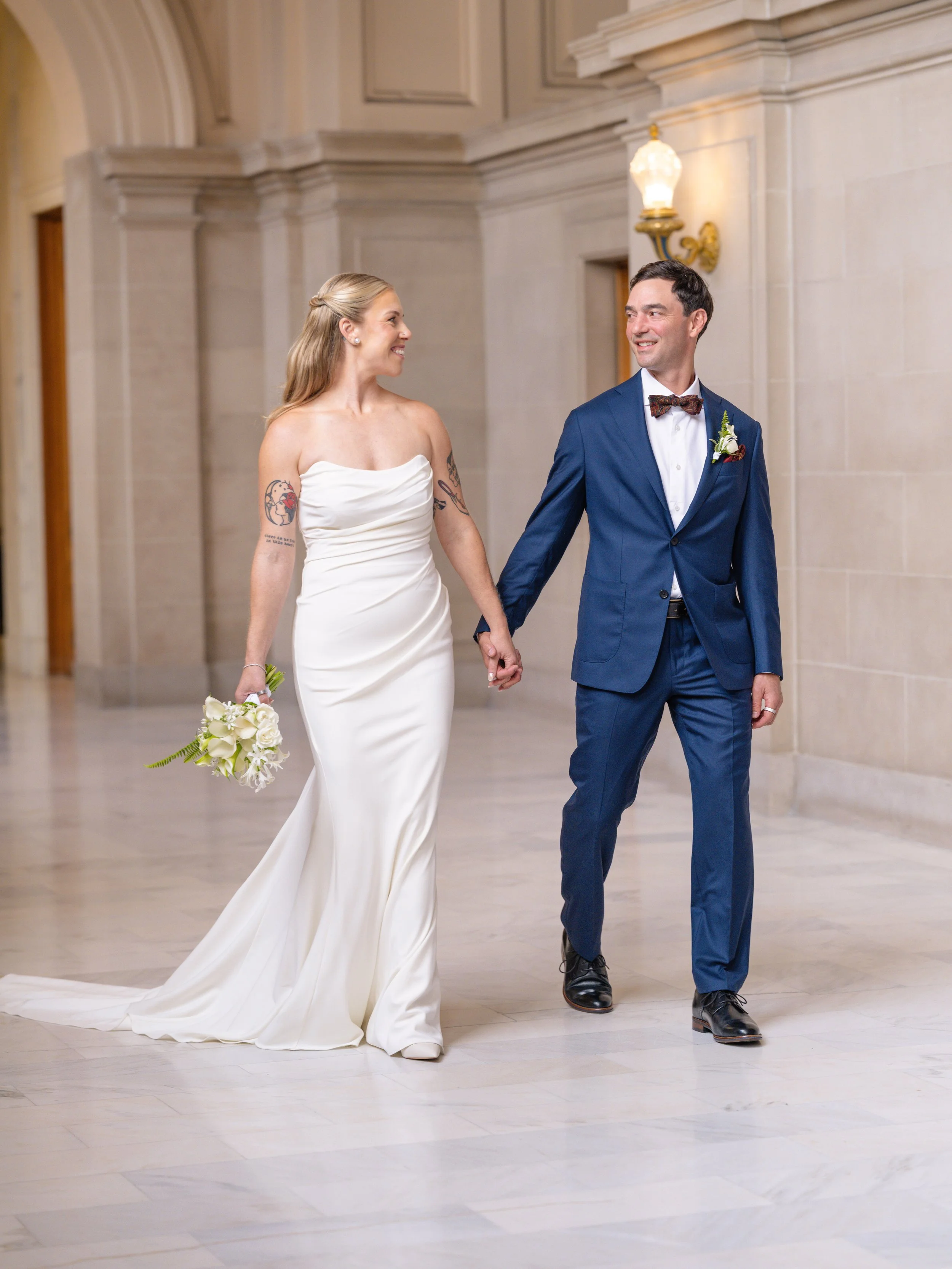 Newlyweds walking hand in hand through an San Francisco city hall, bride carrying an elegant bouquet by Petal and Salt Floral, Bay Area