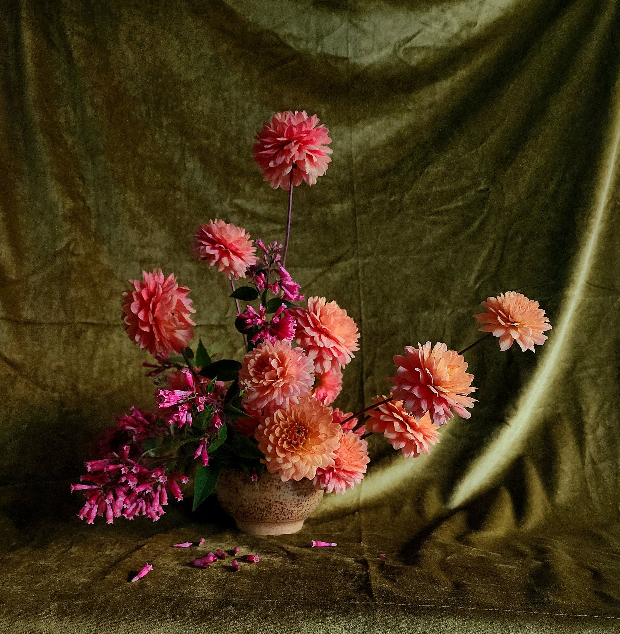 Pink and peach dahlias in a hand made ceramic vase against a moody olive fabric backdrop, Petal + Salt Floral design