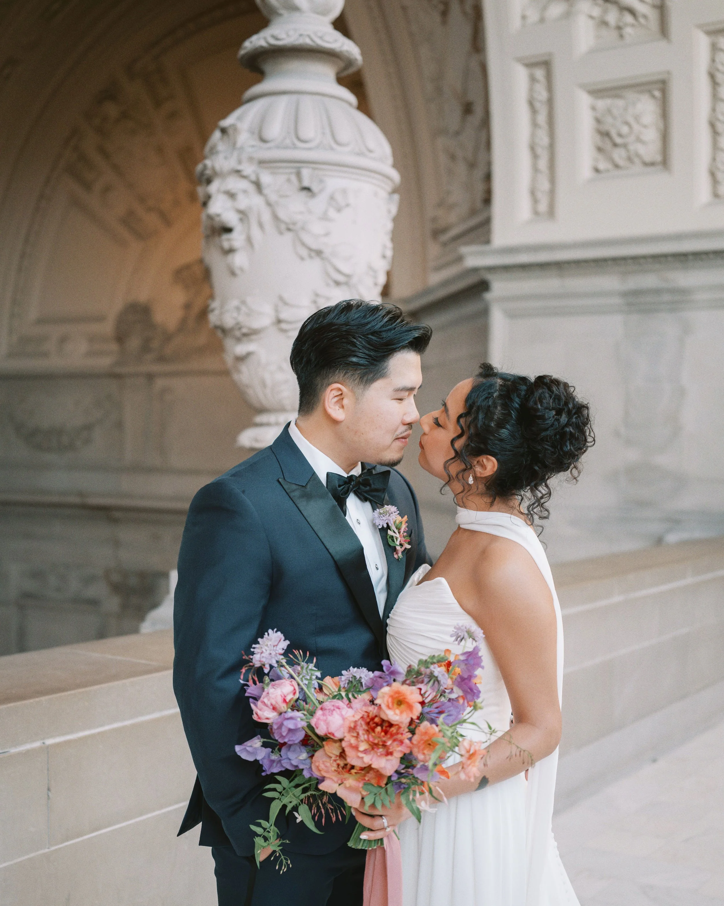 Bride and groom kissing at San Francisco City Hall, bride holding a colorful bouquet by Petal + Salt Floral