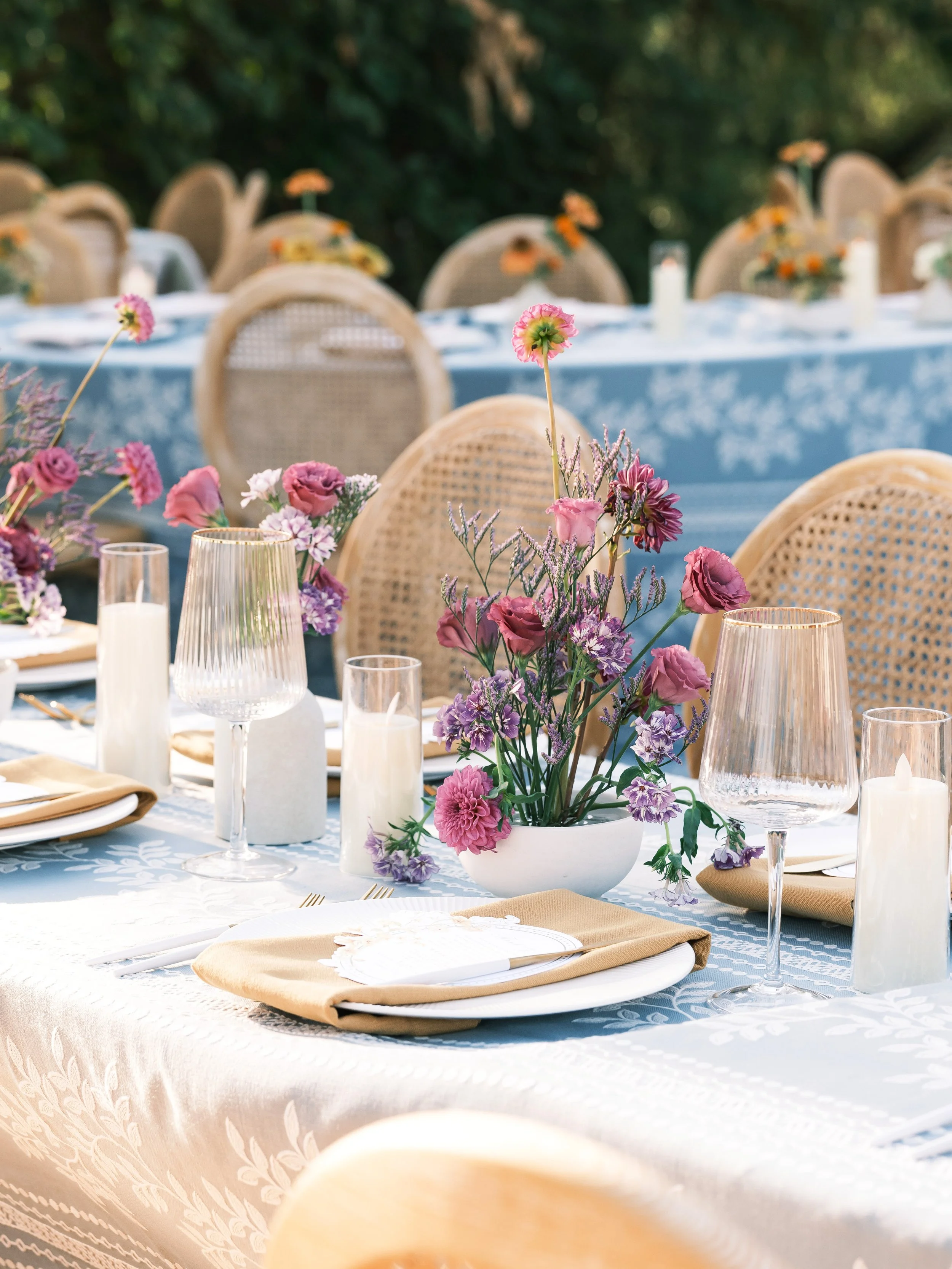 Elegant outdoor dinner table decorated with pink and purple florals, candles, gold flatware, and wine glasses, styled by Petal and Salt Floral
