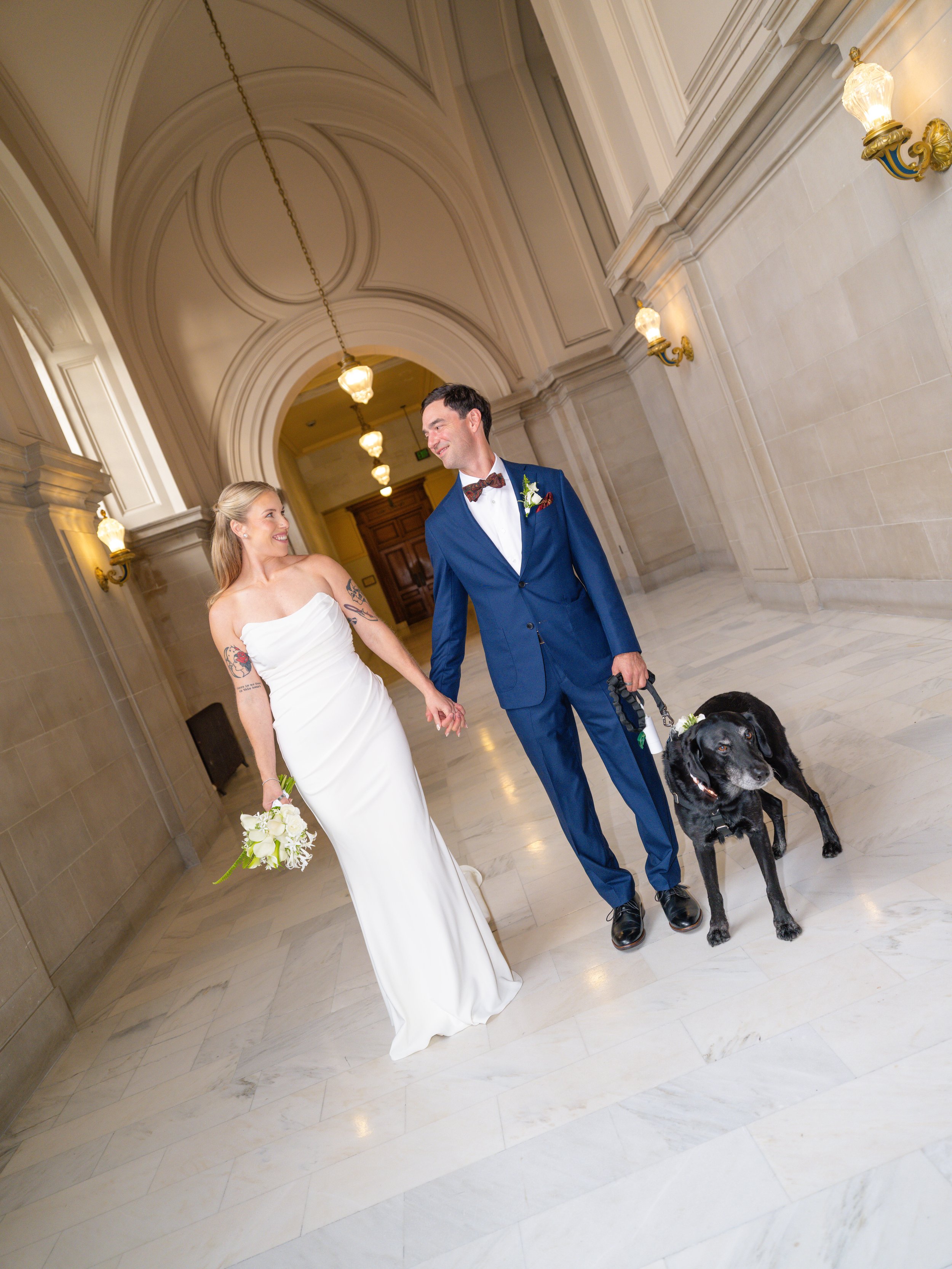 Newlyweds strolling through the grand ornate hallways of San Francisco City hall with their dog, bride holding a bouquet by Petal + Salt Floral