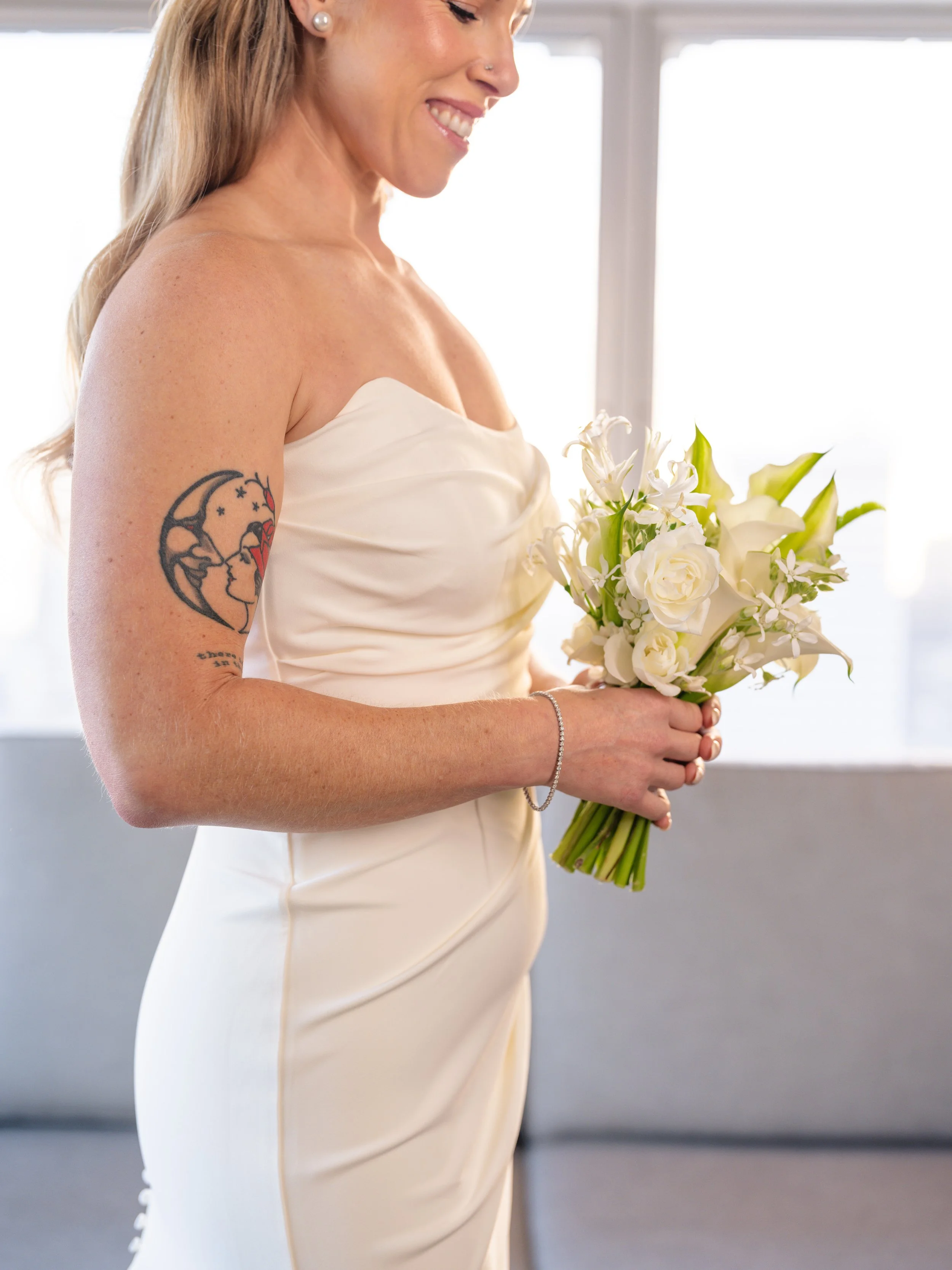 Smiling bride in a strapless wedding gown holding a refined white floral bouquet in her Fairmont San Francisco hotel suite before her wedding vows, Bay Area wedding florist Petal + Salt