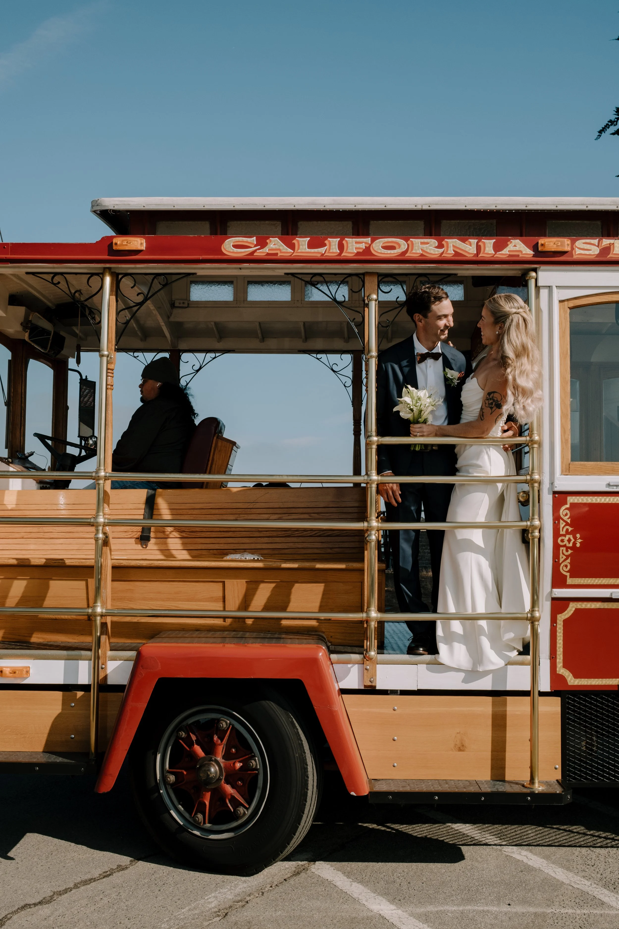 Bride holding a delicate all white floral bouquet while standing with her groom on a vintage California trolley after their San Francisco City Hall wedding ceremony, wedding florals by Petal and Salt Floral