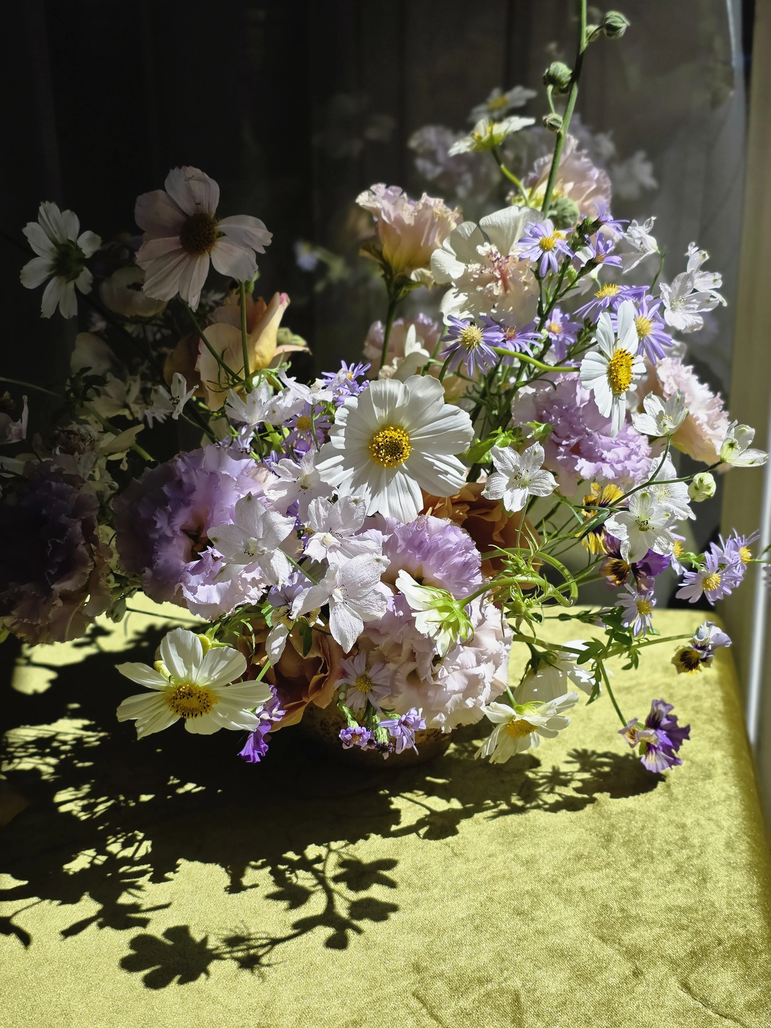 Still-life style floral arrangement with bold sunlit shadows cast across a green surface, Petal + Salt Floral