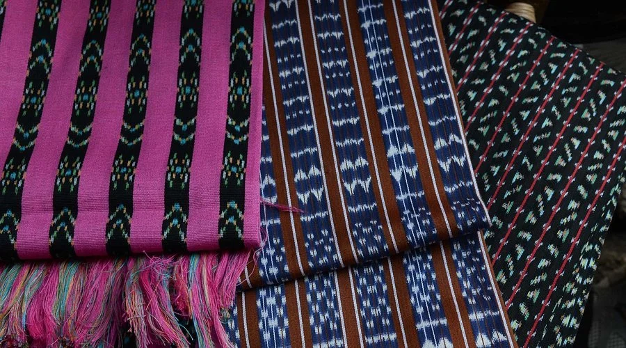 Three handmade woven textiles with colorful striped patterns on a flat surface.
