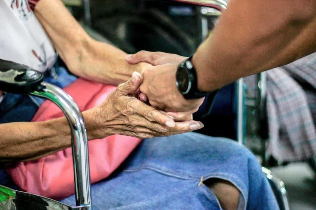 young man clasps the hands of elderly woman in wheelchair