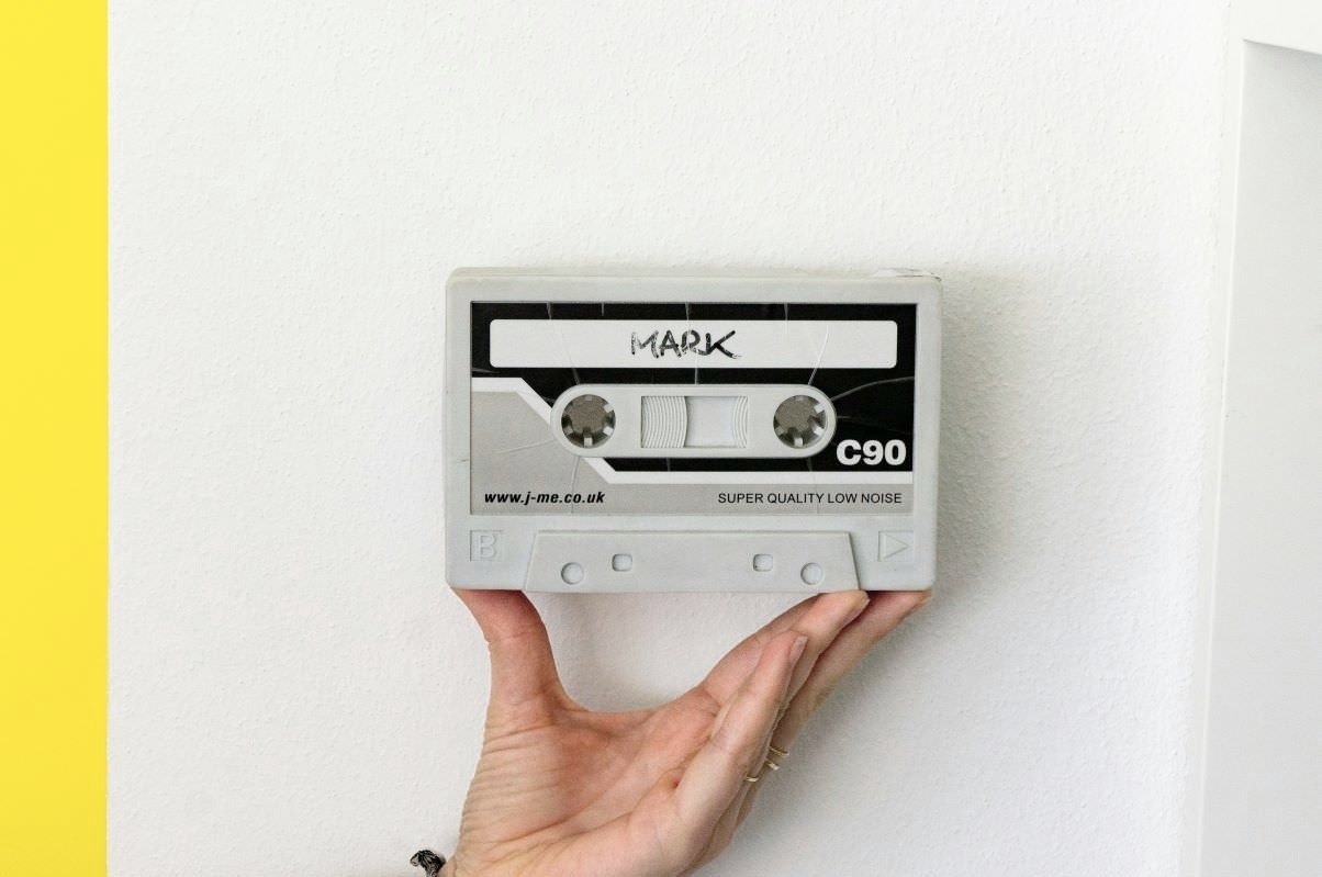 woman's hand holds up audio cassette with handwritten name Mark on label