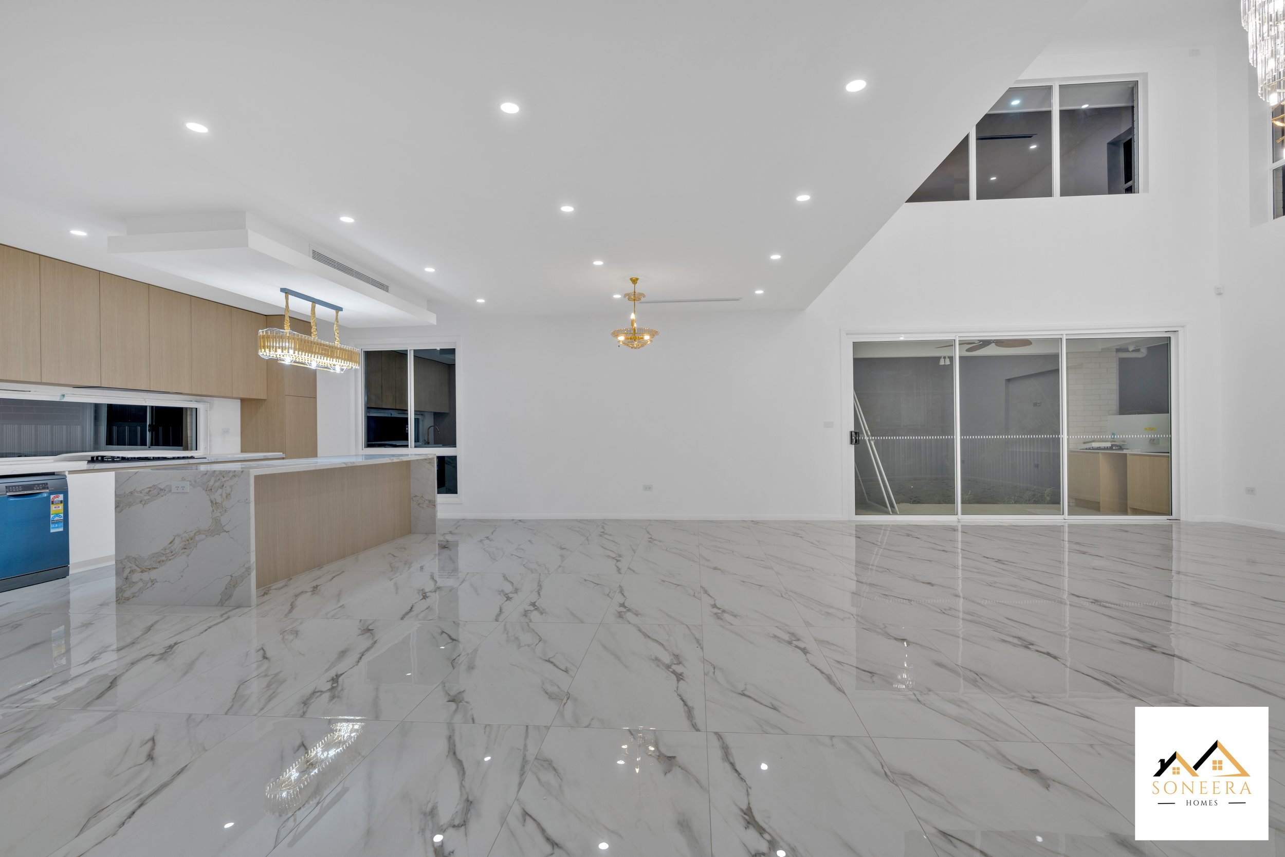 Empty modern living space with white marble floors, white walls, a kitchen counter with marble accents, large windows, and a balcony door.