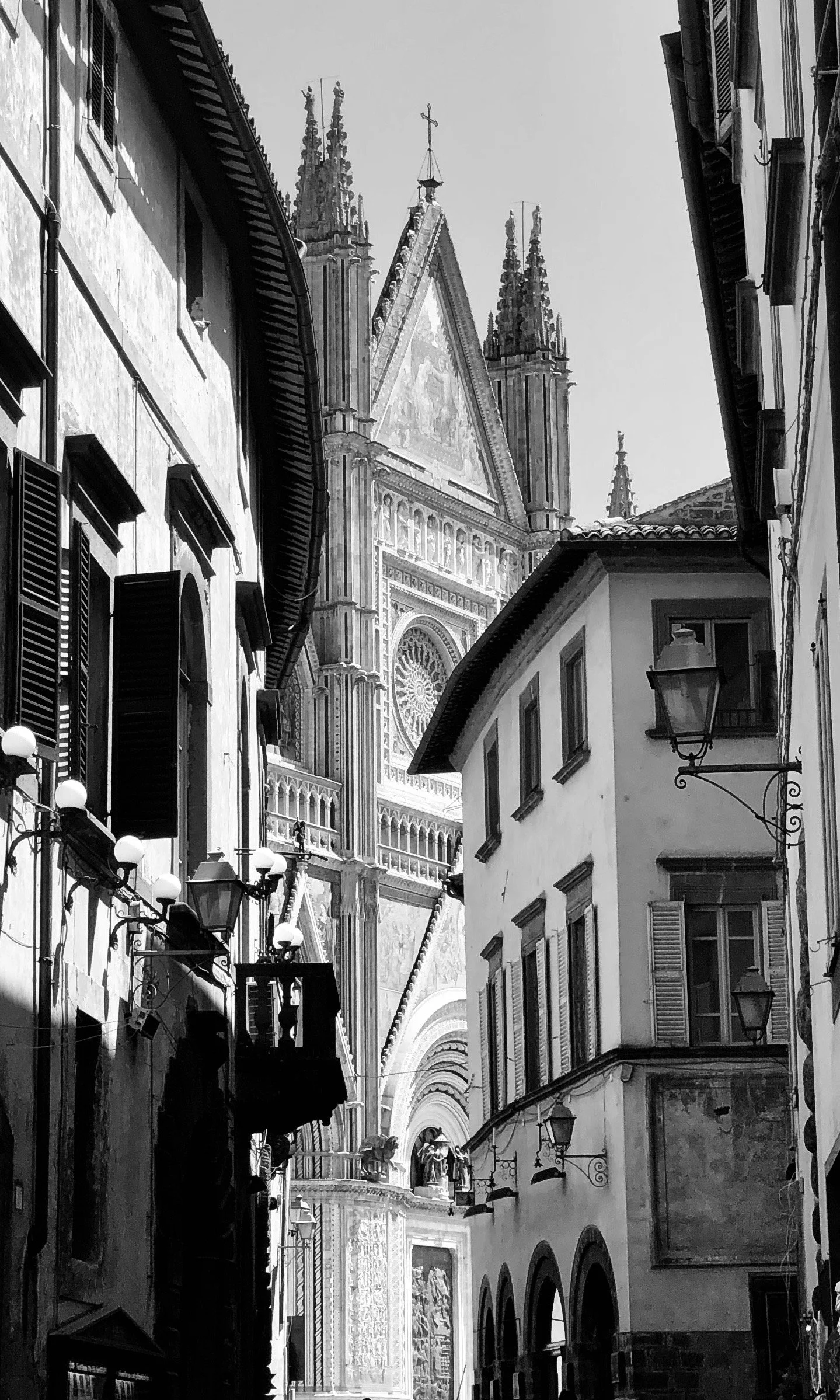 Black and white photo of a narrow street with classic European-style buildings and a large church in the background, featuring detailed architecture and a gothic façade.