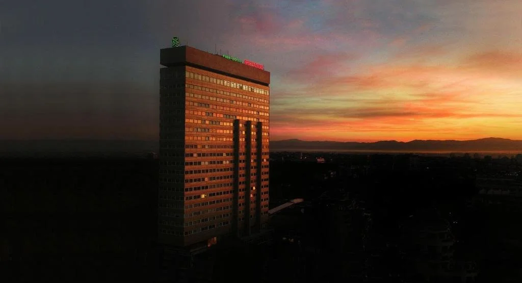 Tall office building at sunset, with mountains in the distance and colorful sky.