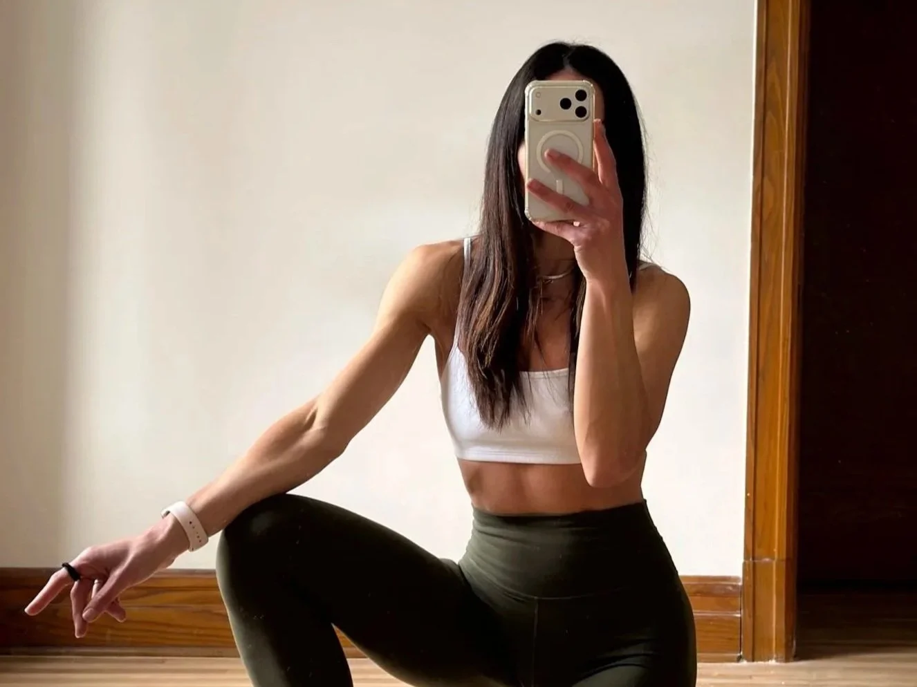 vêtement à genou sur son tapis d'entraînement dans son salon en legging vert kelly et un haut noir à manche longue avec des dumbbell de 3lbs dans les mains