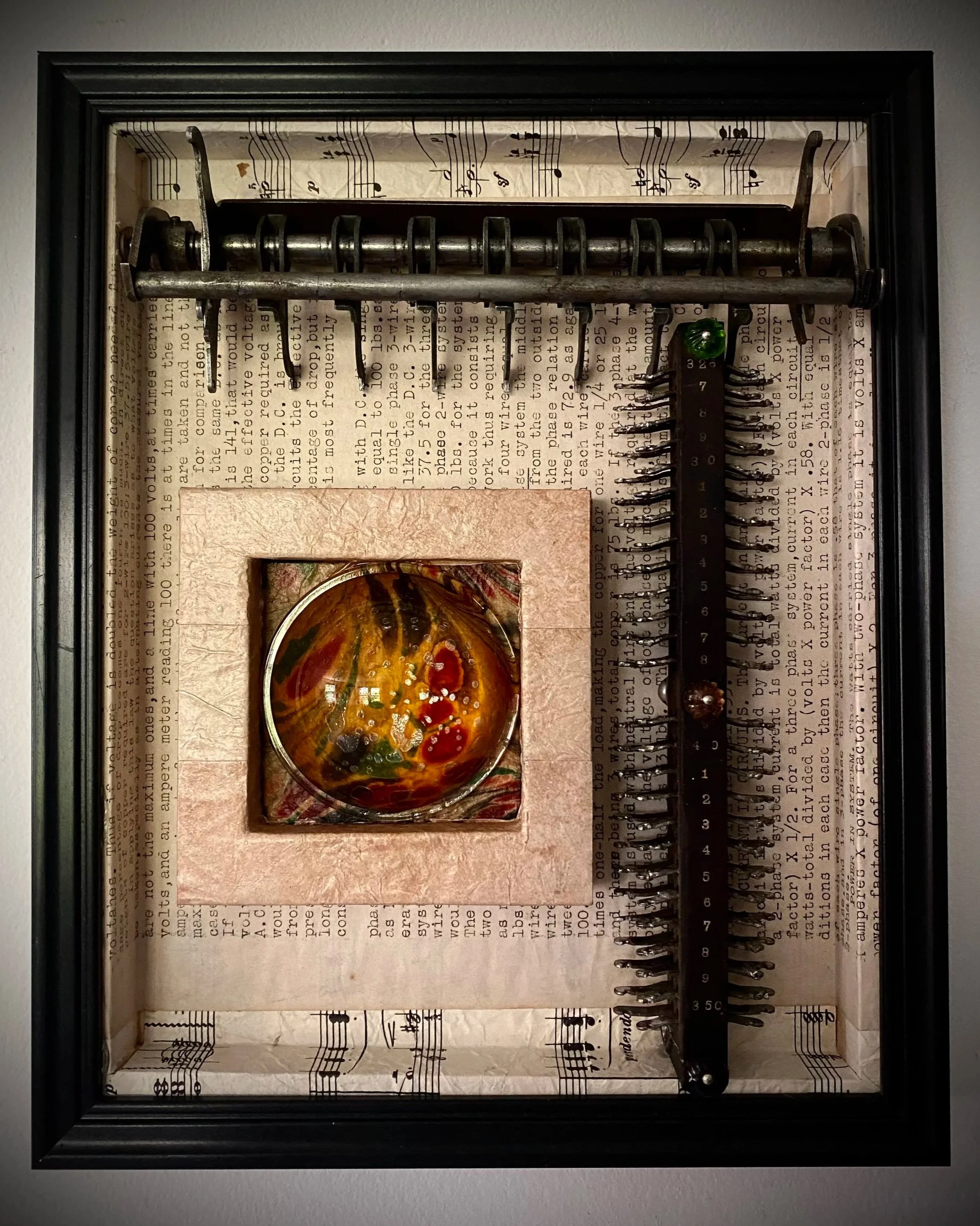 Assemblage artwork featuring vintage electronic components and a colorful glass centerpiece within a shadow box frame.