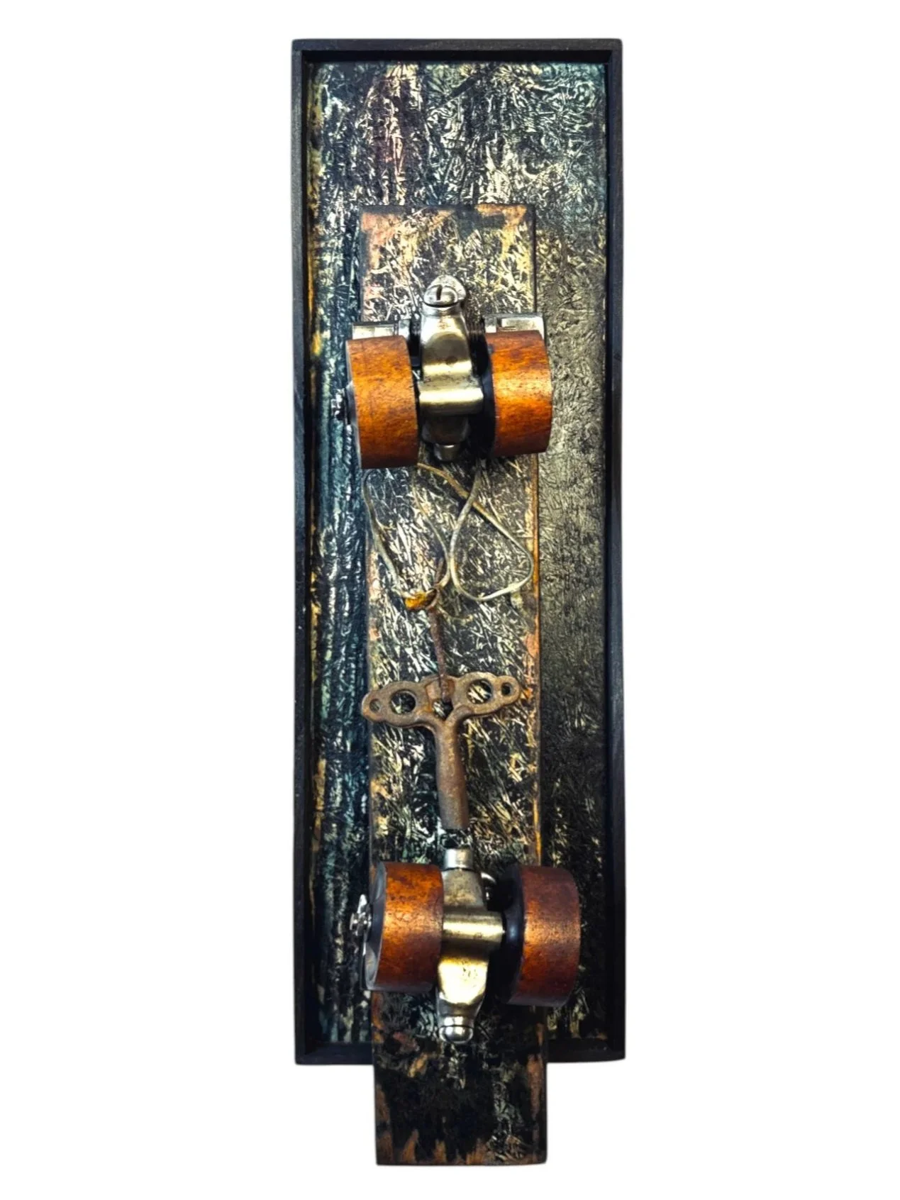Skate Lock Memory – vertical assemblage artwork featuring vintage roller skate wheels, a prominent skate key with looped wire, and layered wooden framing in earthy tones