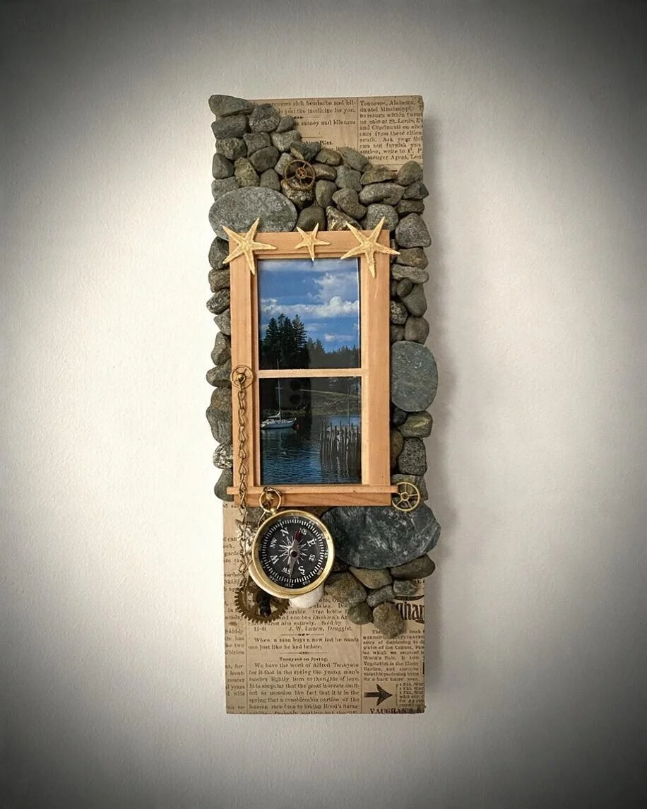 Maine Coastal Views VI: Quiet Harbor, mixed-media assemblage by Kharris B featuring a Maine harbor photograph, beach stones, starfish, vintage gears, compass, and wooden window frame.