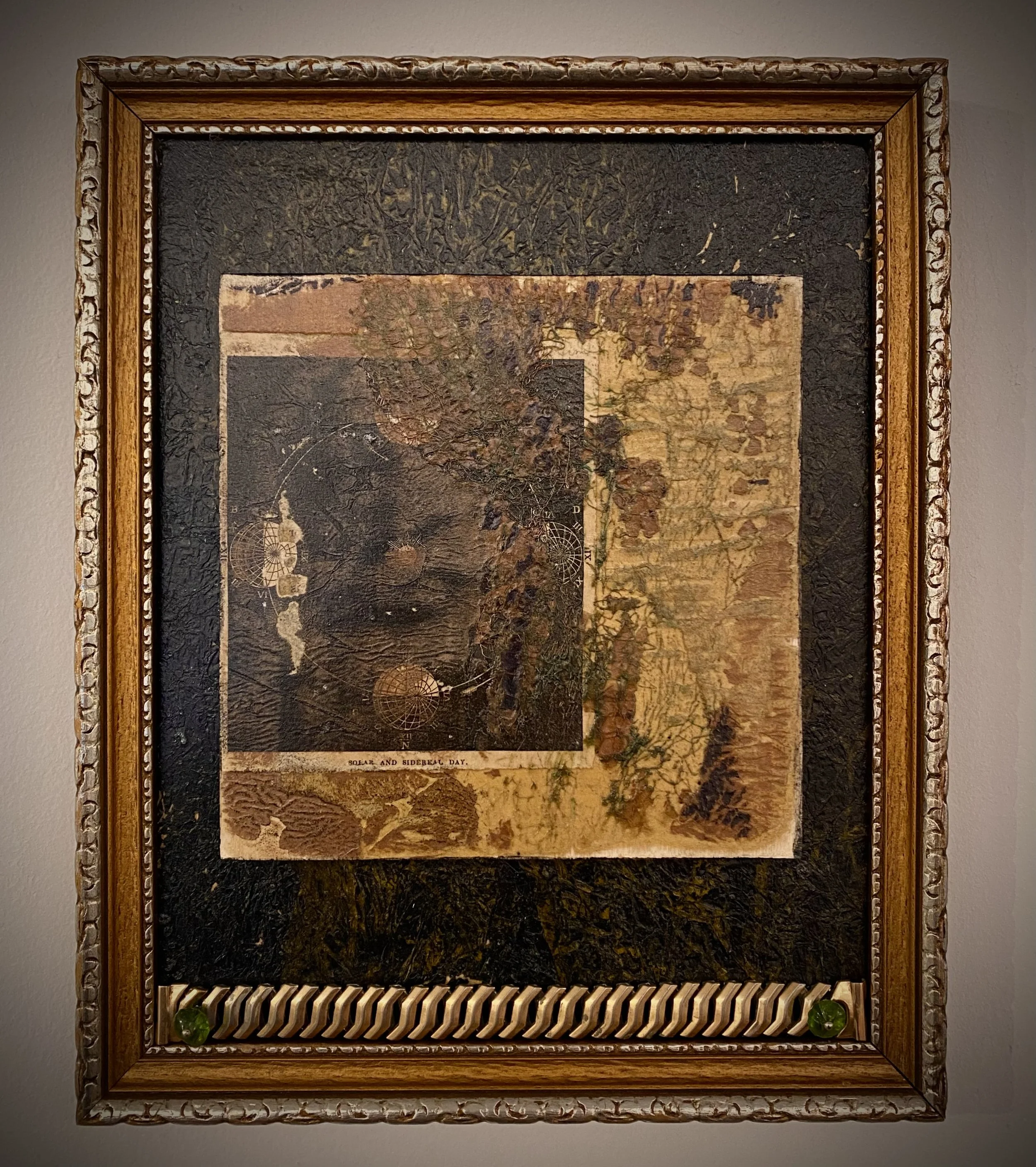 Mixed media assemblage featuring layered vintage printed papers and textured surfaces within an ornate gold frame.