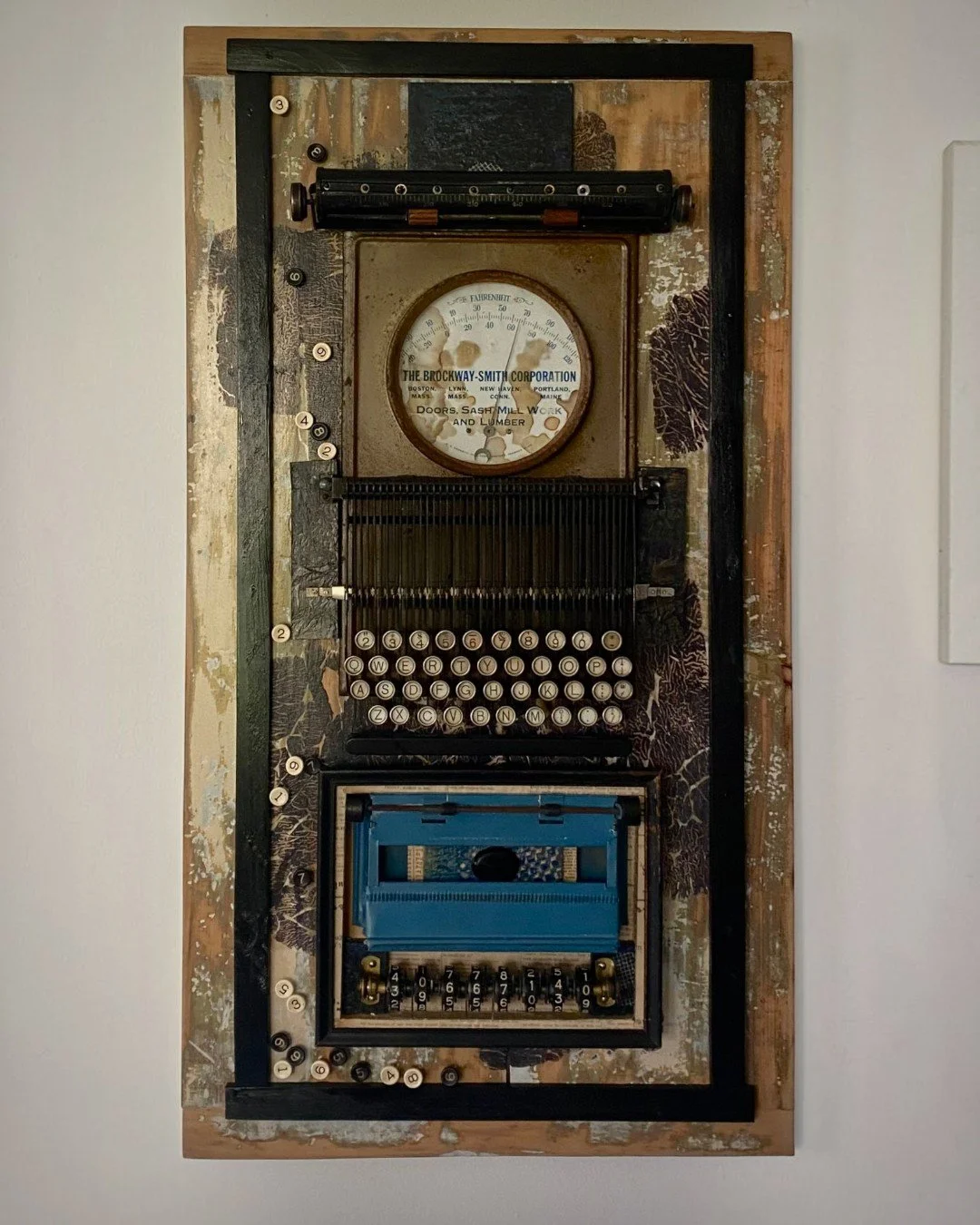 Assemblage artwork featuring vintage typewriter components, a mechanical calculator, and an industrial gauge mounted on layered reclaimed materials.