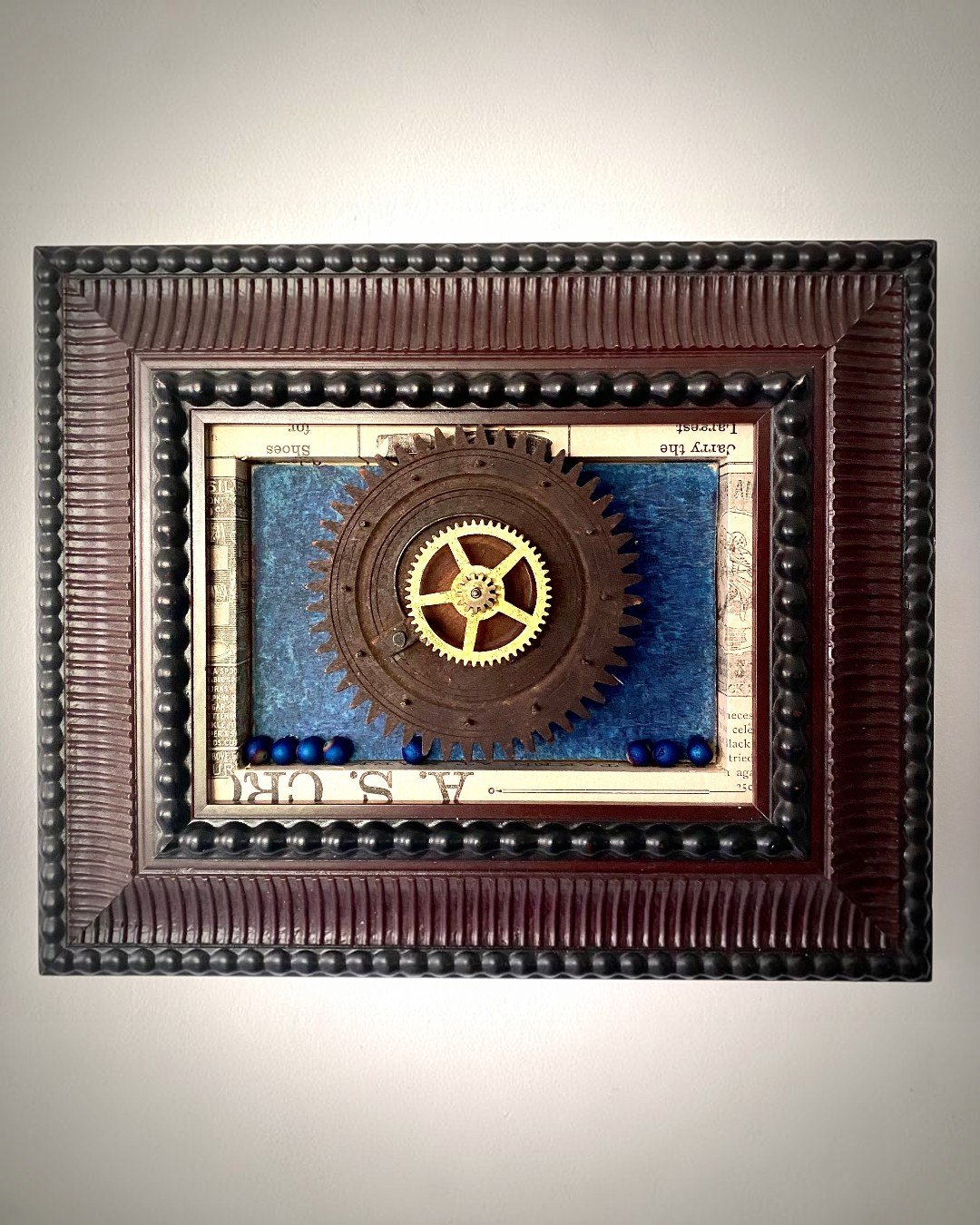 Assemblage artwork featuring a large vintage gear centered against layered blue textured surfaces.