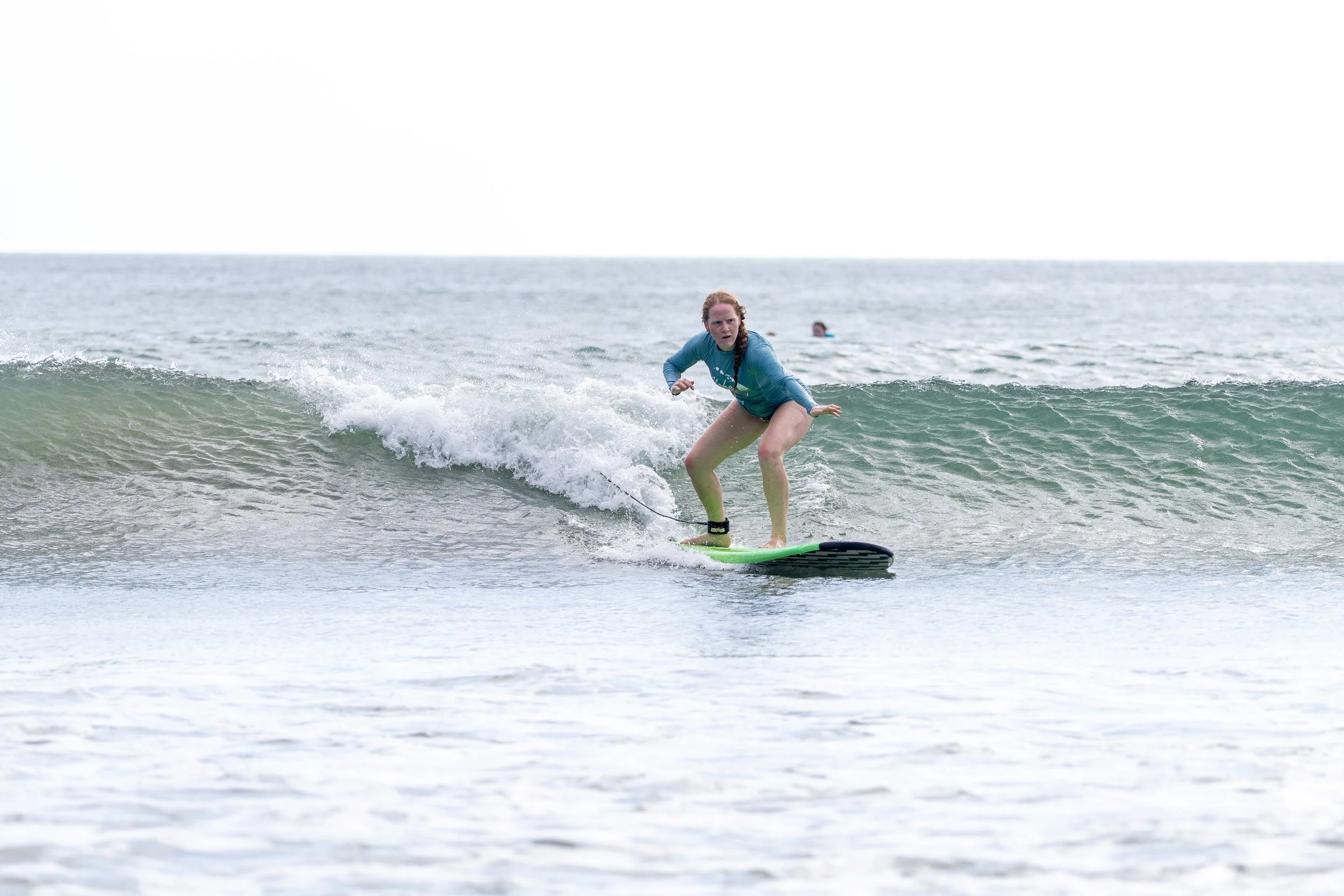 A woman surfboarding on a small wave in the ocean with a person swimming in the background.