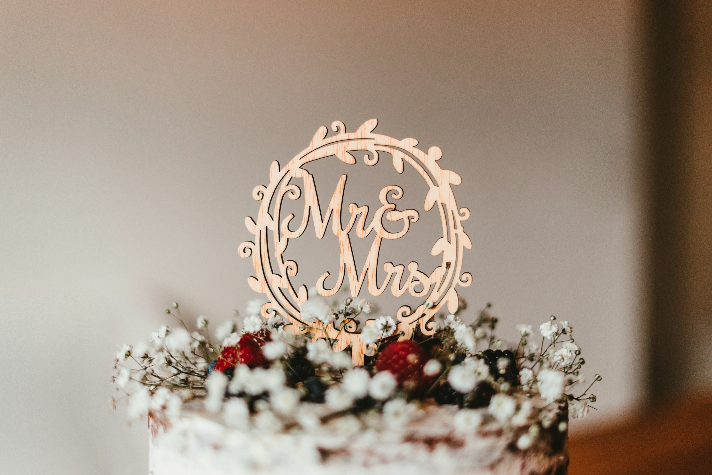 Cake with a decorative topper reading 'Mr & Mrs' surrounded by white baby's breath flowers and berries.