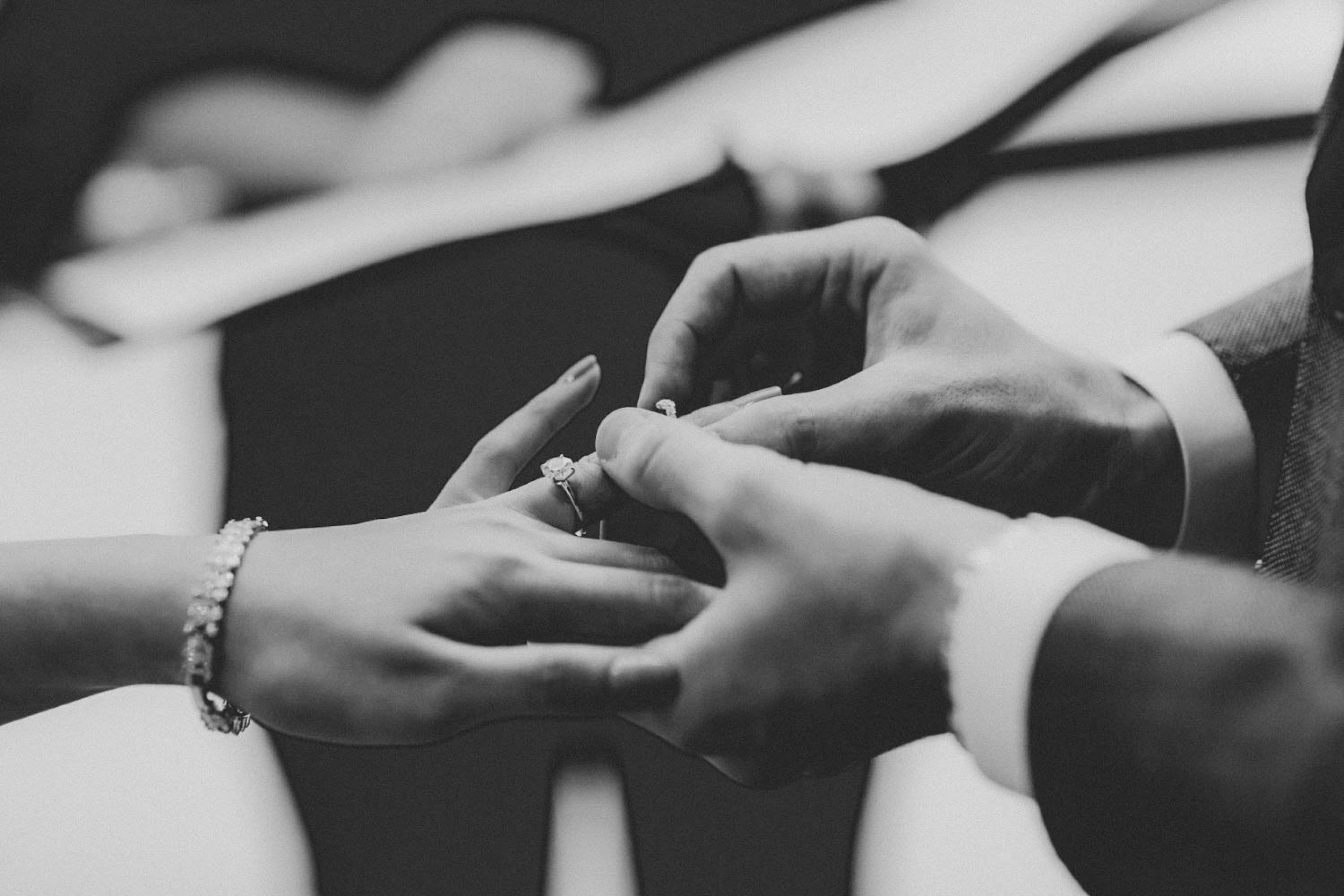 Black and white photo of a person placing a wedding ring on a woman's finger during a wedding ceremony.
