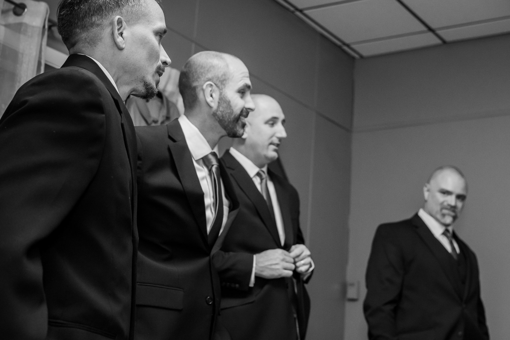 Four men in suits standing in a line against a wall, engaged in a formal or professional setting.
