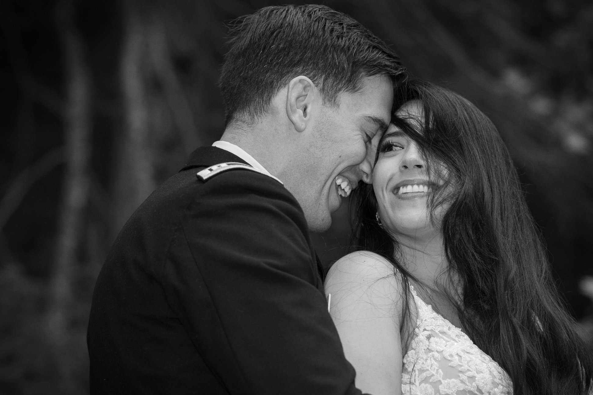 A black and white photo of a man in a military uniform and a woman smiling and touching foreheads, both showing joy and affection.