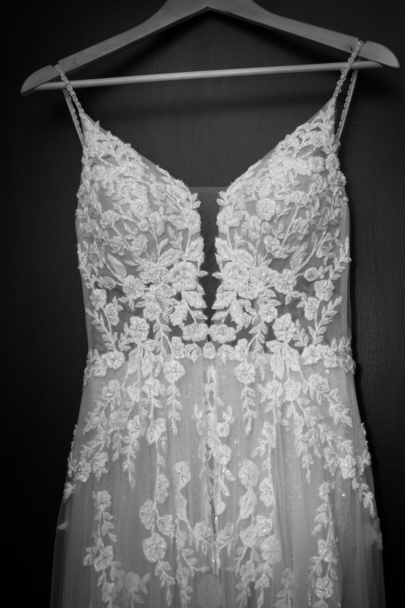 A wedding dress with floral lace appliqué hanging on a hanger.